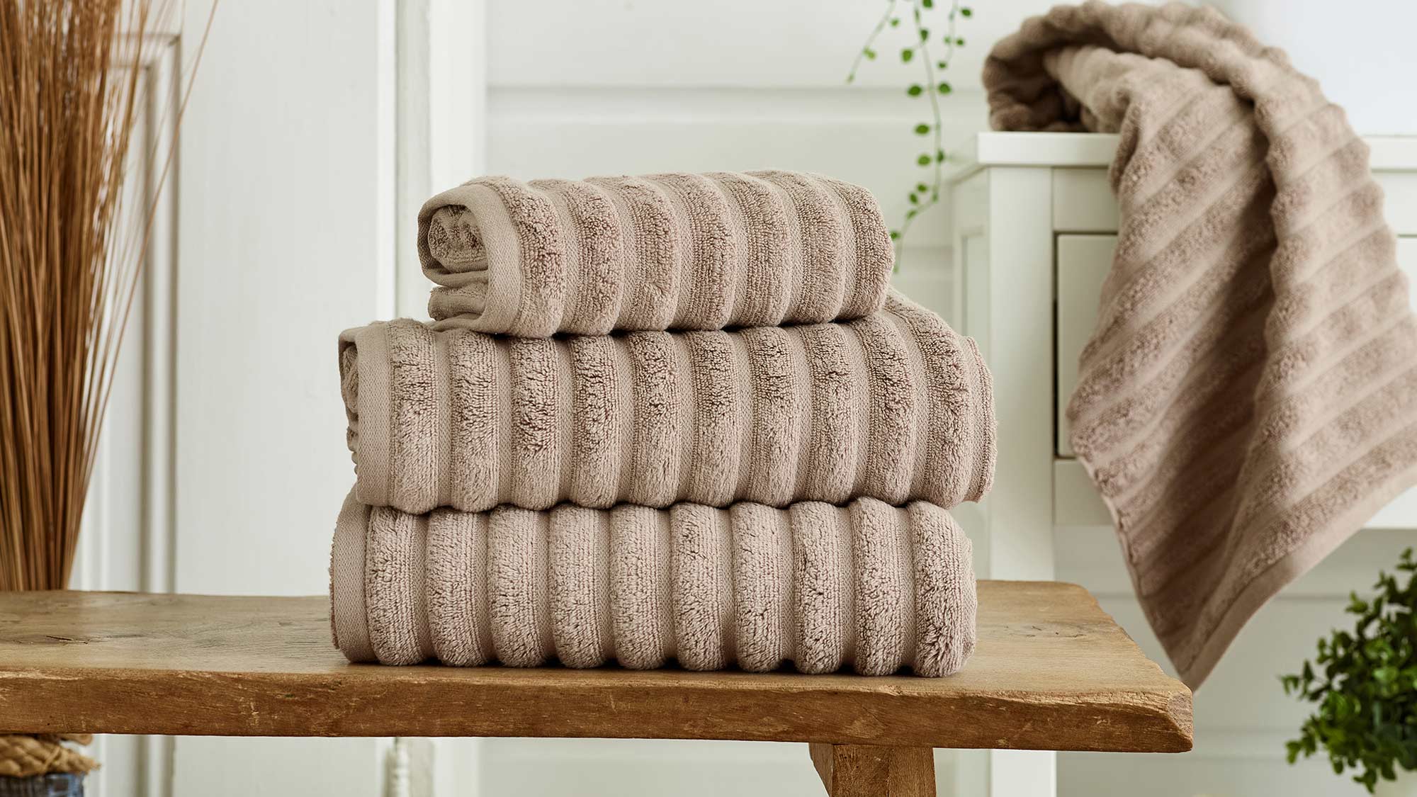Stack of folded beige towels on a wooden bench in a bathroom setting.