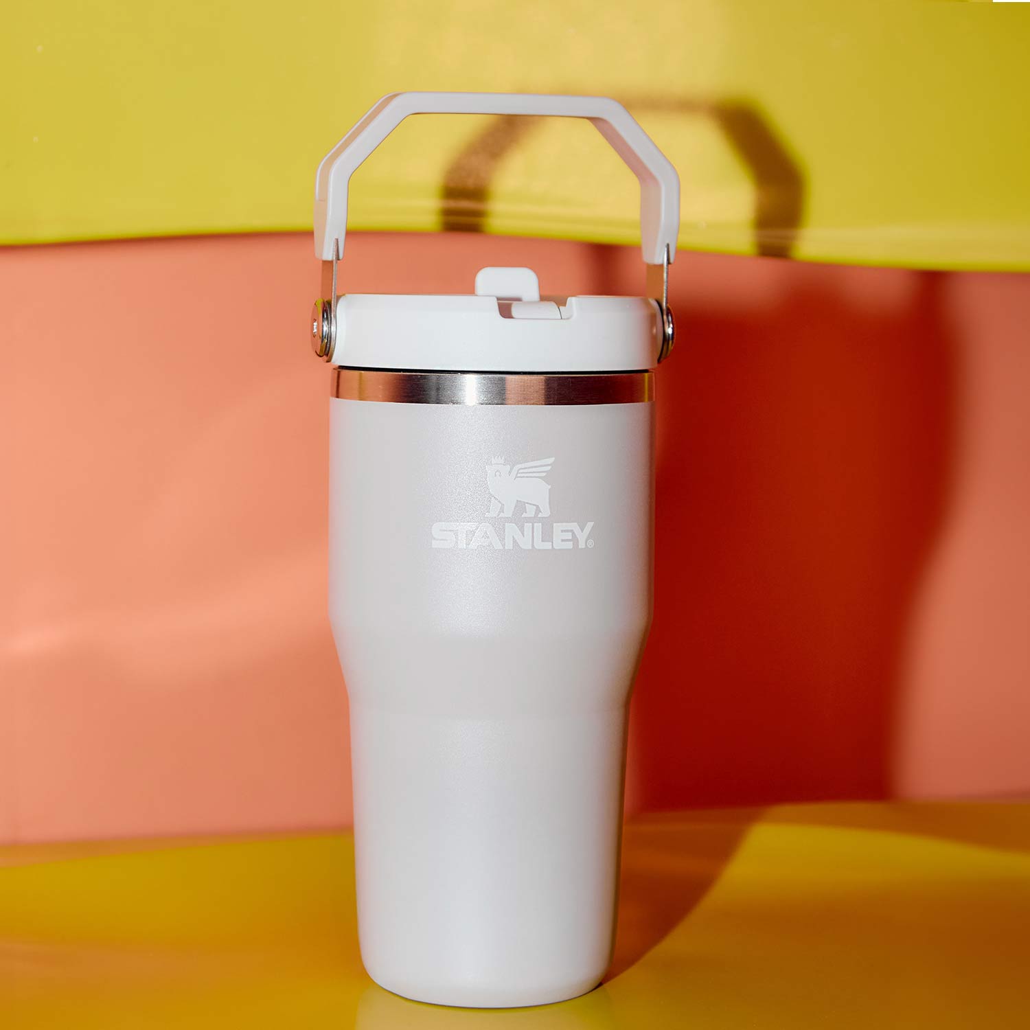 White Stanley insulated tumbler with handle and metal band on coloured background