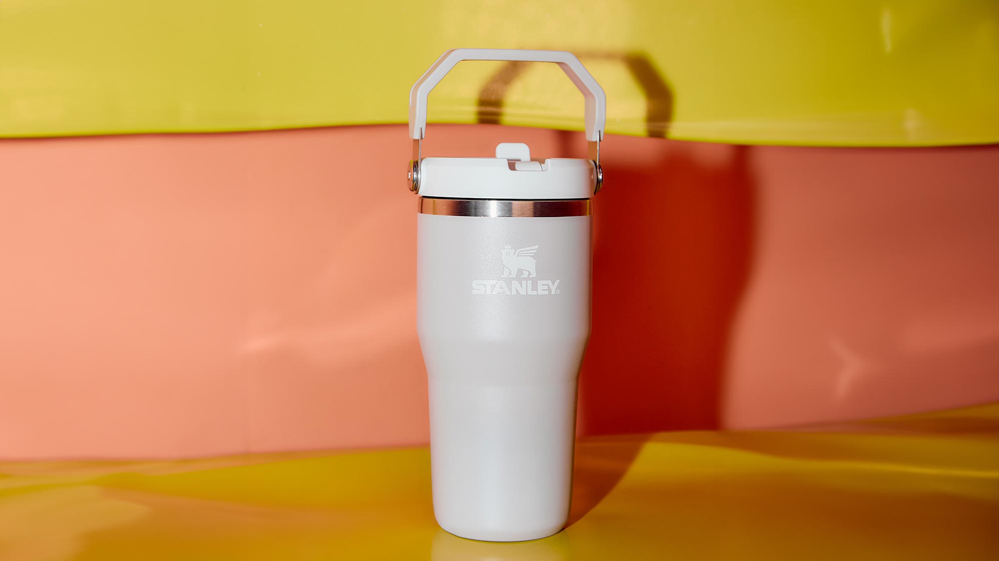 White Stanley insulated tumbler with handle and metal band on coloured background