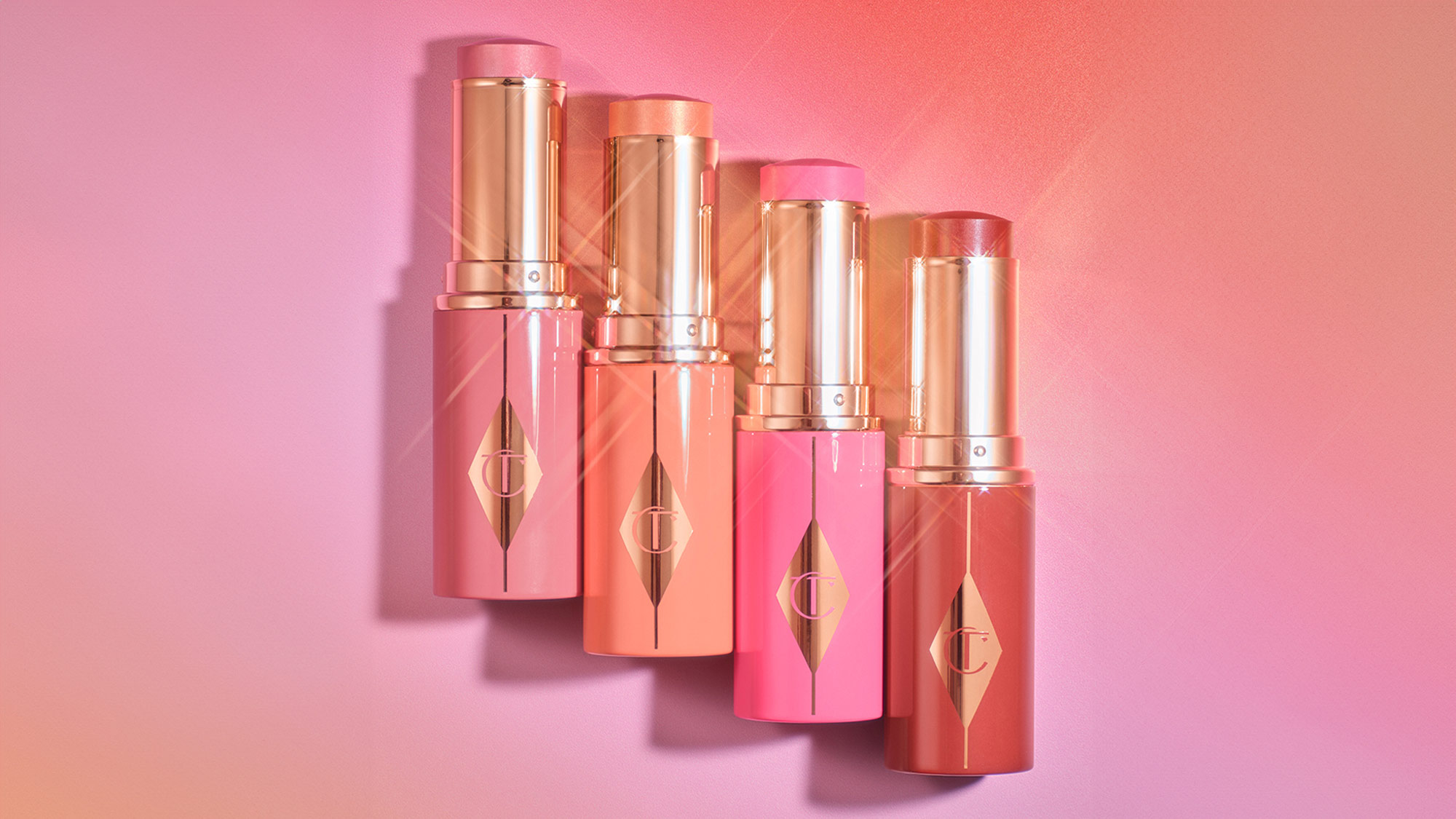 Four tubes of Charlotte Tilbury blusher with gold caps on a gradient pink background.