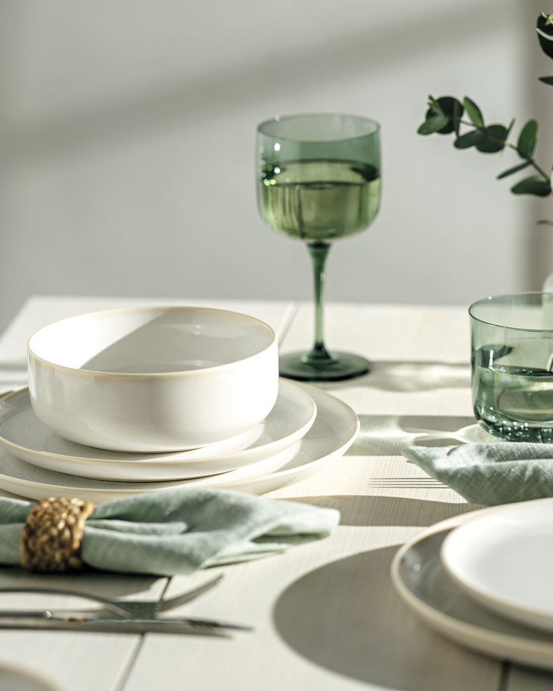 Elegant table setting with a white bowl, green glassware, and a light green napkin on a textured surface.