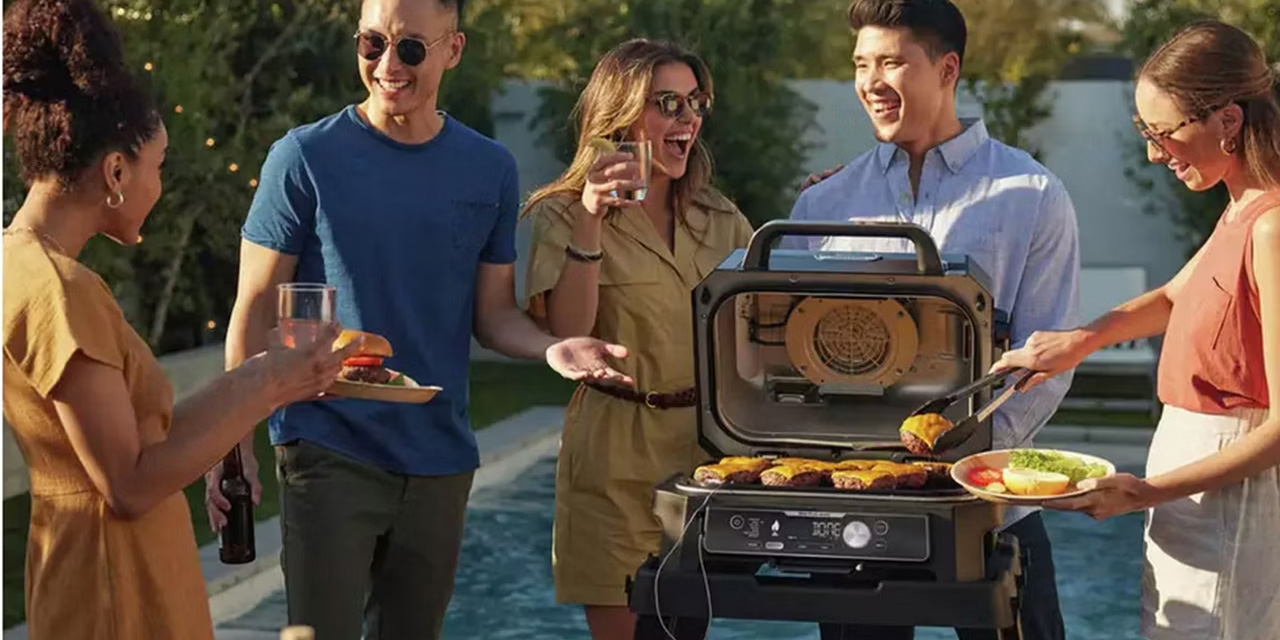 A group of friends grilling and enjoying drinks by a pool, using a Ninja brand grill.