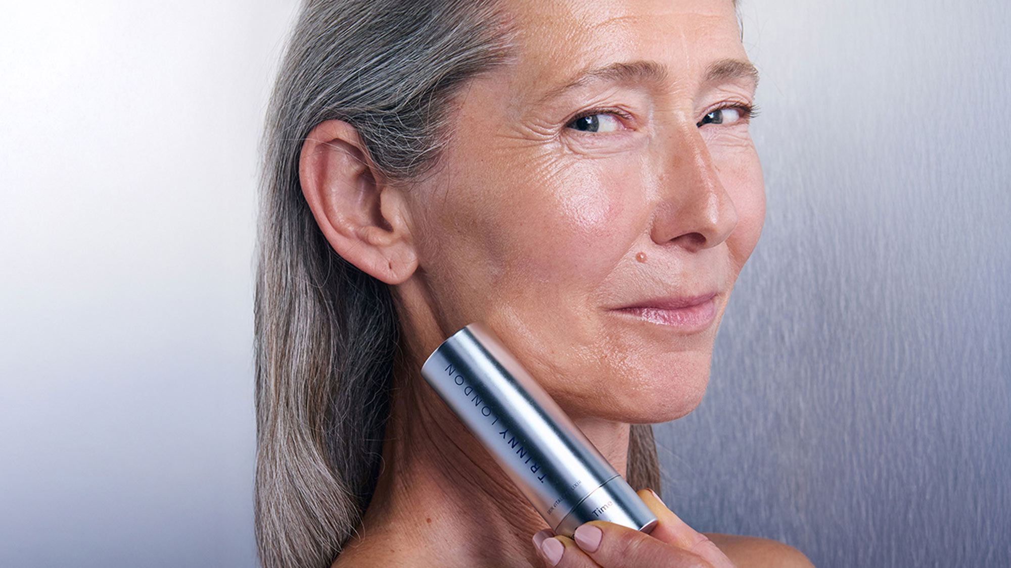 A person applying Trinny London skincare product to their neck.
