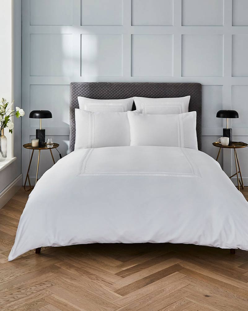 Elegant bedroom with a white bed, gray headboard, and side tables with lamps, set against a paneled wall.