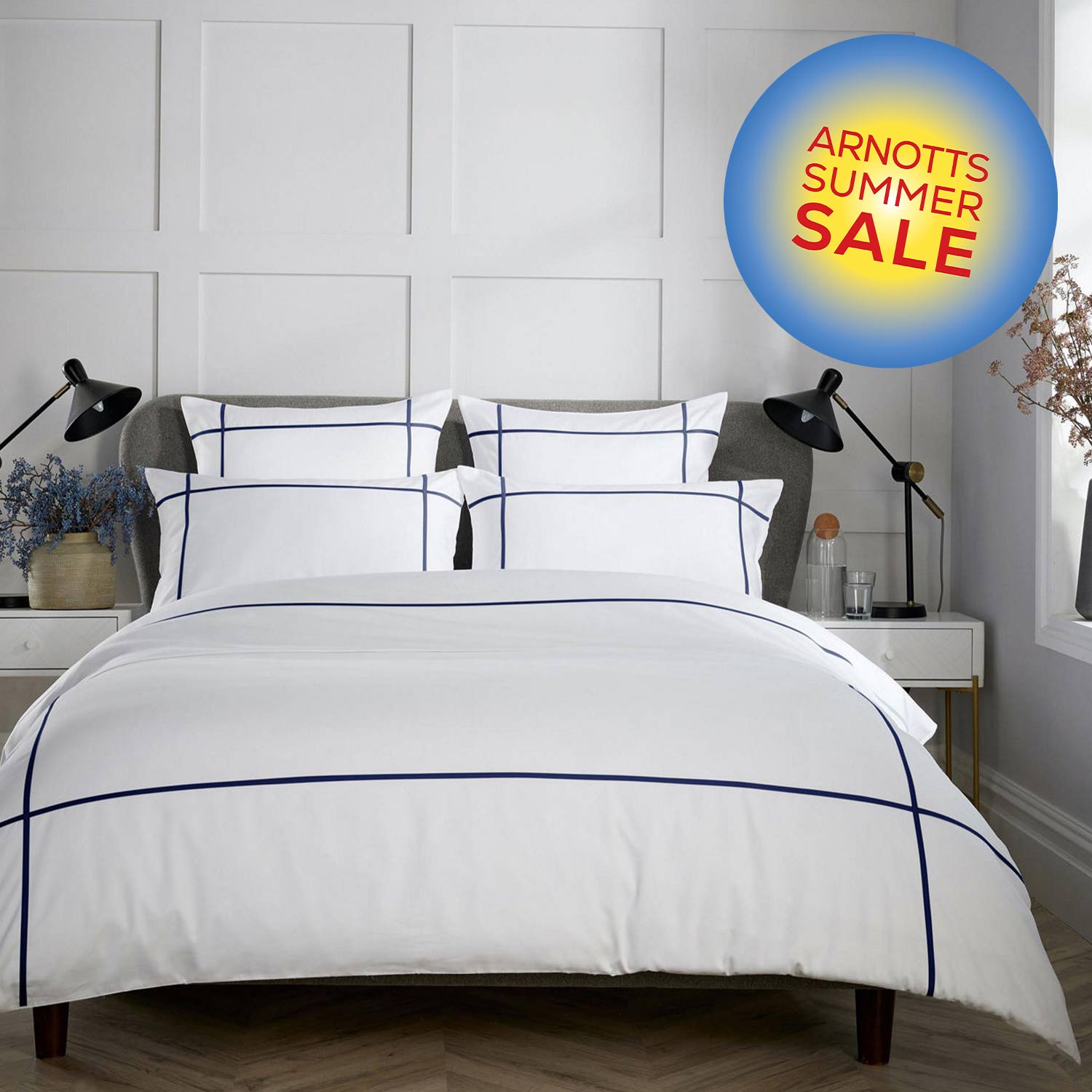 Modern bedroom with a neatly made bed, white and navy geometric bedspread, black lamps, and decorative plants.