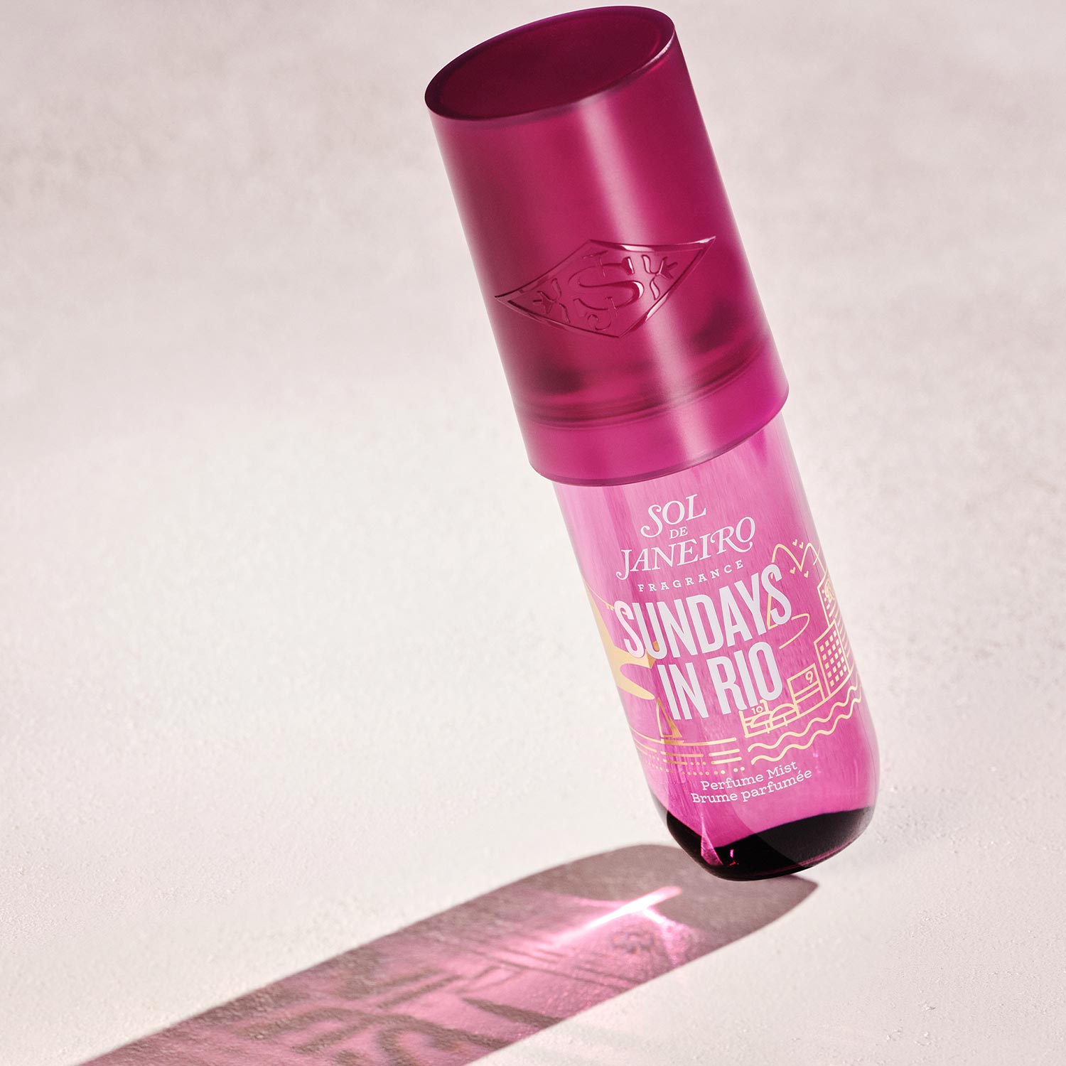 A pink perfume bottle labeled 'Sol de Janeiro, Sunday's in Rio,' casting a shadow on a light surface.