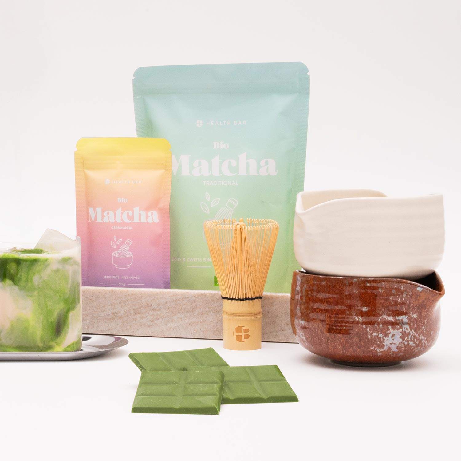 A variety of matcha tea products, including powdered tea, a whisk, and a cup, arranged on a white surface.
