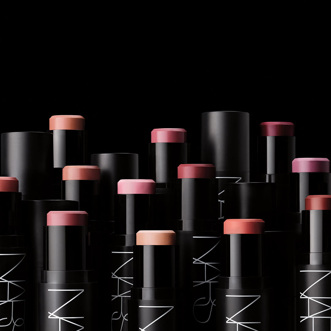 Several tubes of NARS lip products in varying shades, arranged diagonally on a black background.