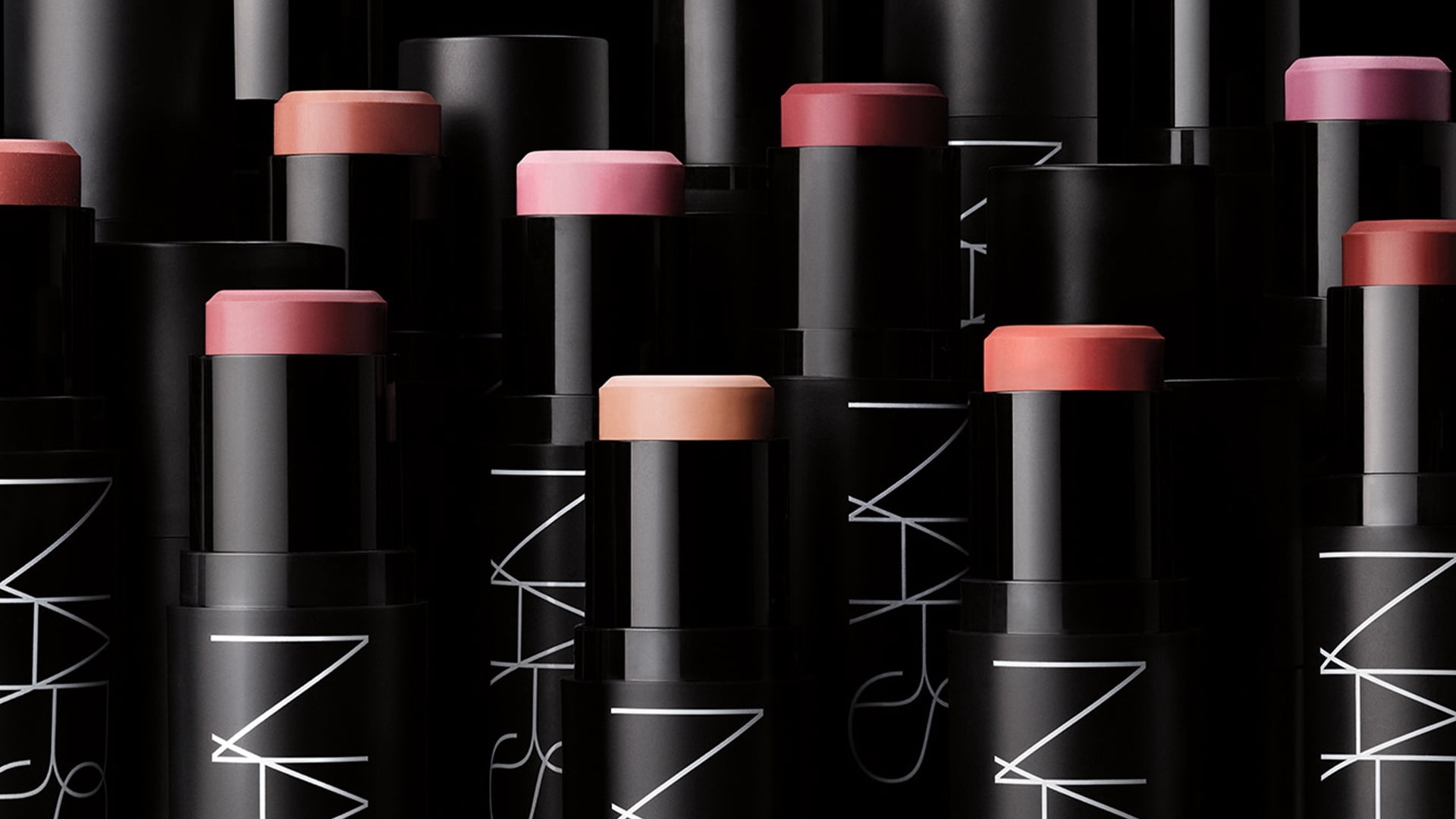 Several tubes of NARS lip products in varying shades, arranged diagonally on a black background.