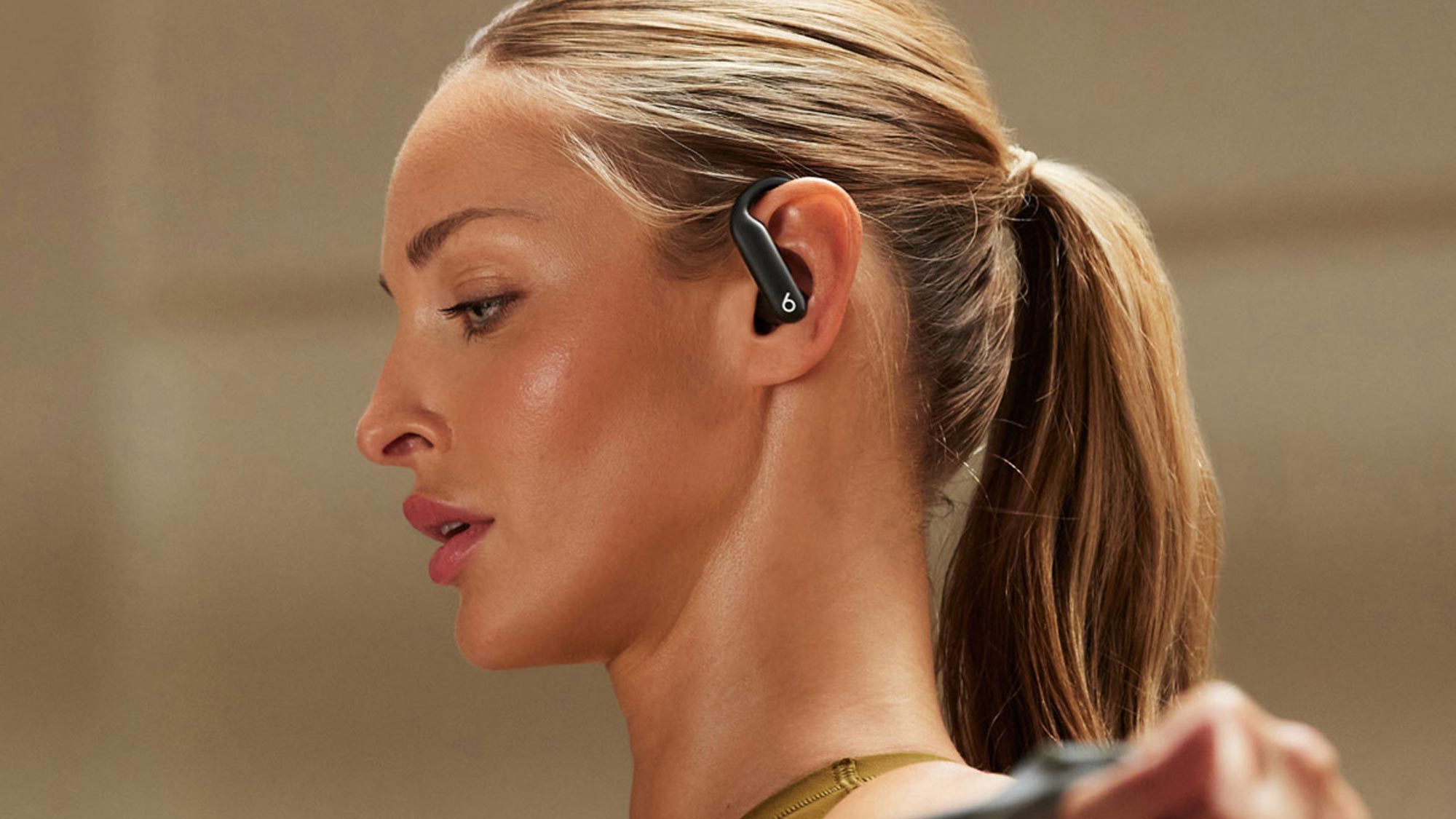 A woman wearing earbuds exercises with a resistance band, her hair in a ponytail.