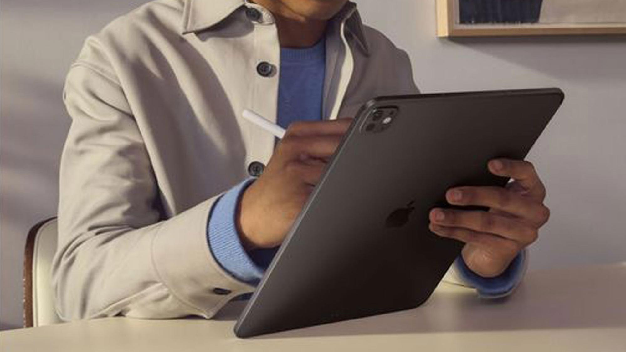 Person using a tablet with a stylus, seated indoors, focused on the screen.