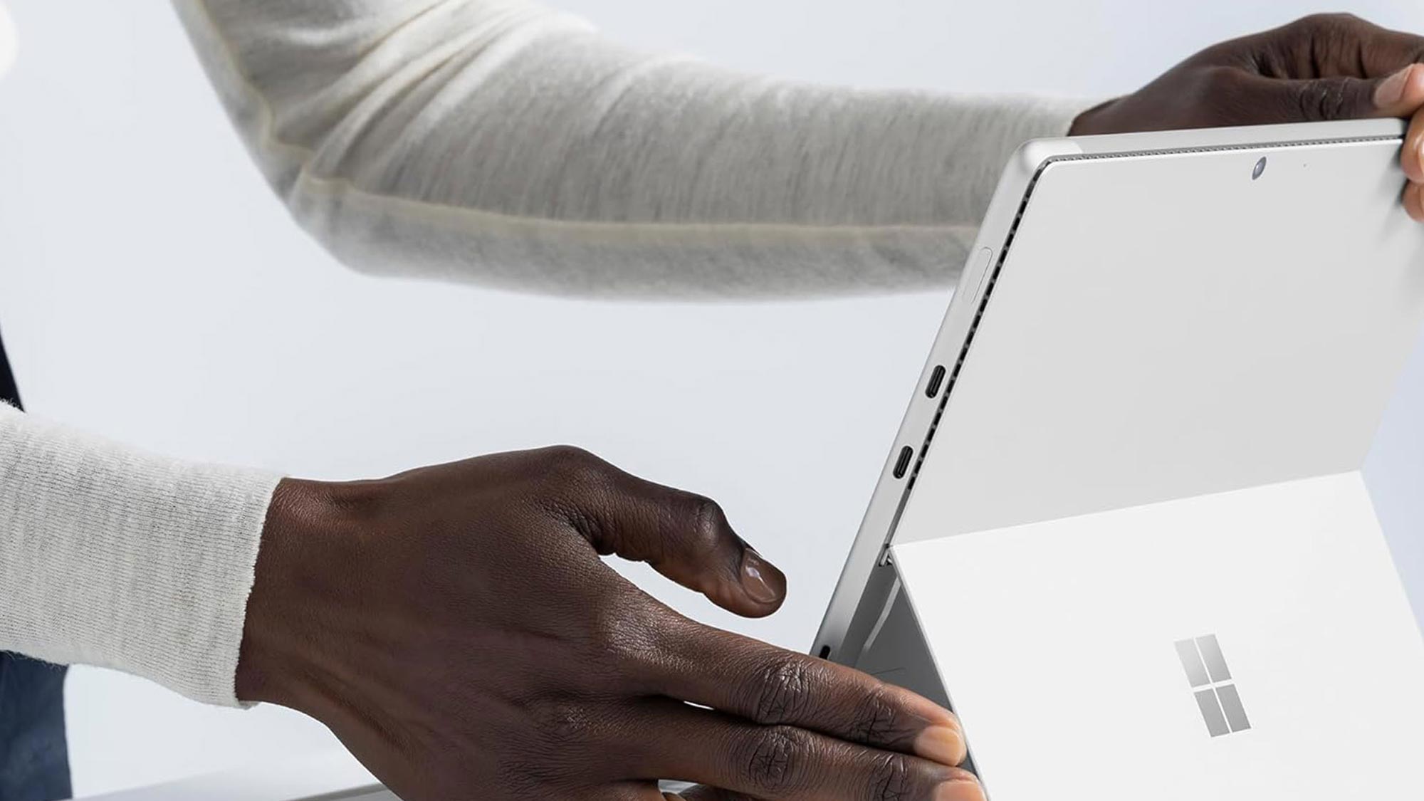 A person adjusting a white tablet with a stand, next to a stylus on a table.