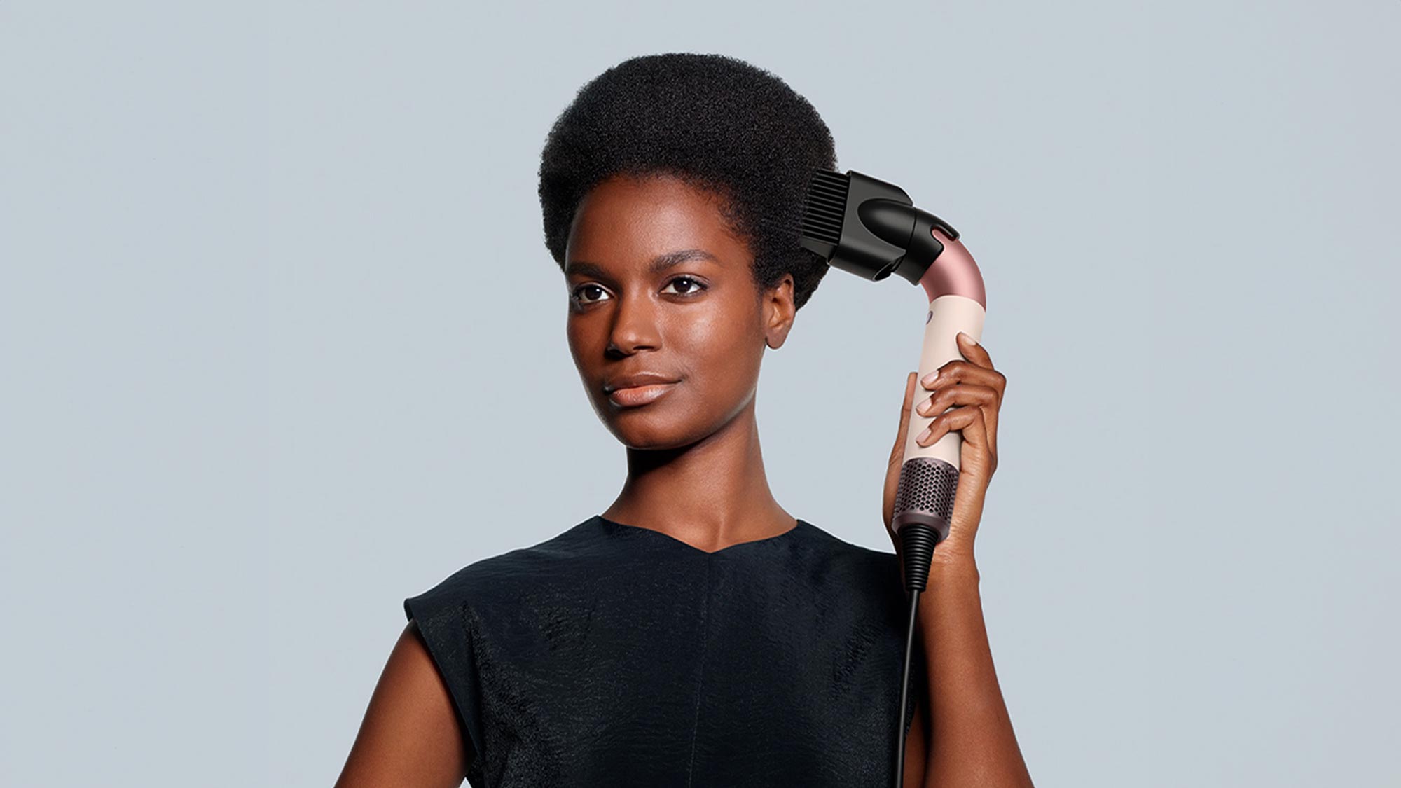 A person is using a hair styling tool, holding it near their hair.
