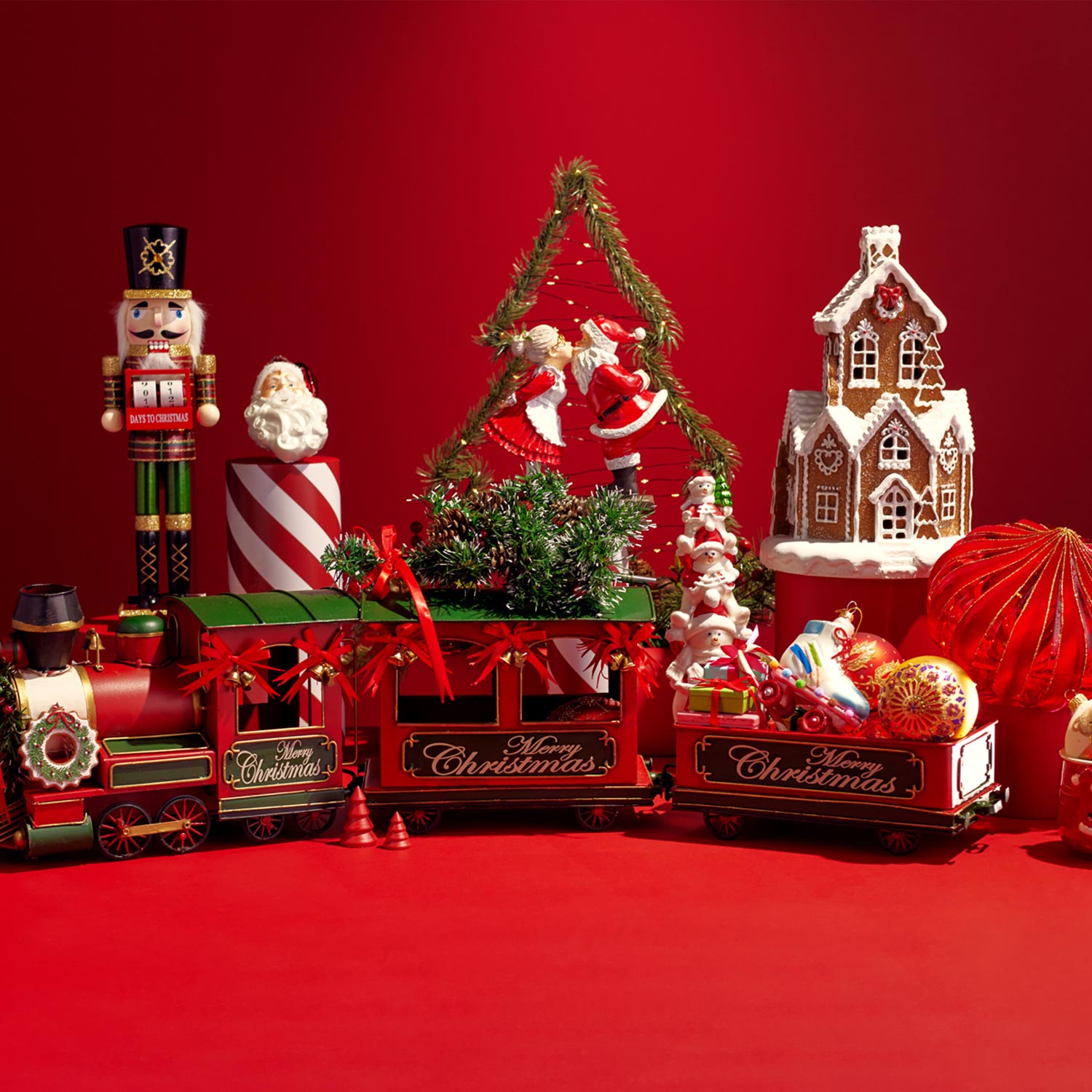 Christmas-themed decorations with a toy train, nutcracker, gingerbread house, santa, and ornaments on a red background.