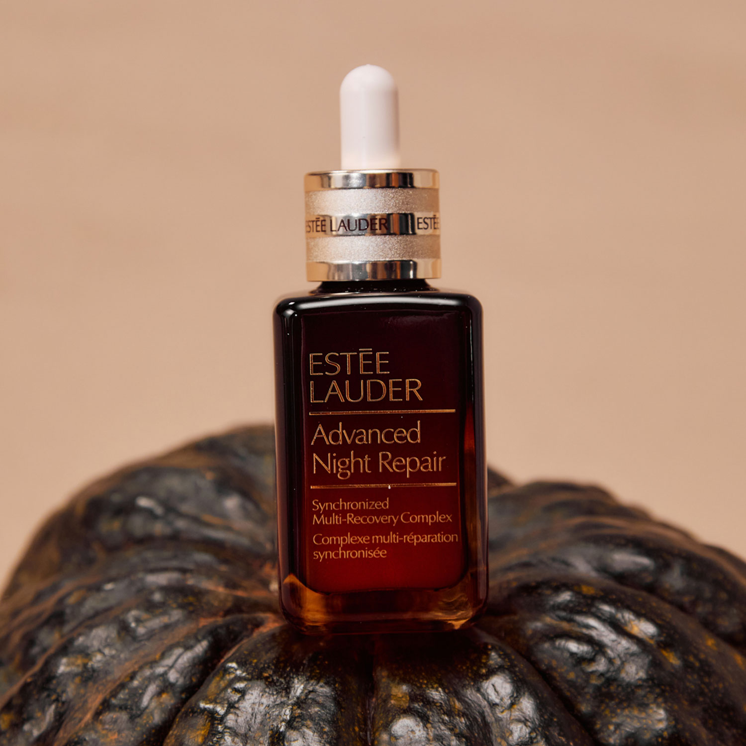 A bottle of Estée Lauder Advanced Night Repair is placed on a dark pumpkin.