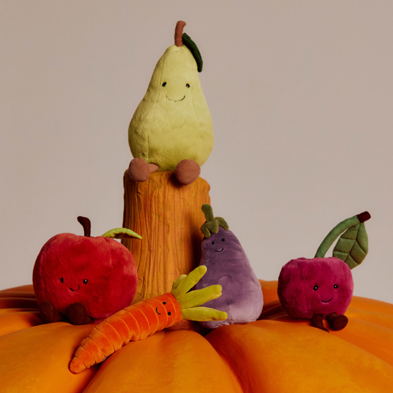 A large pumpkin with small plush fruits and vegetables on top, including a pear, apple, carrot, and radish.