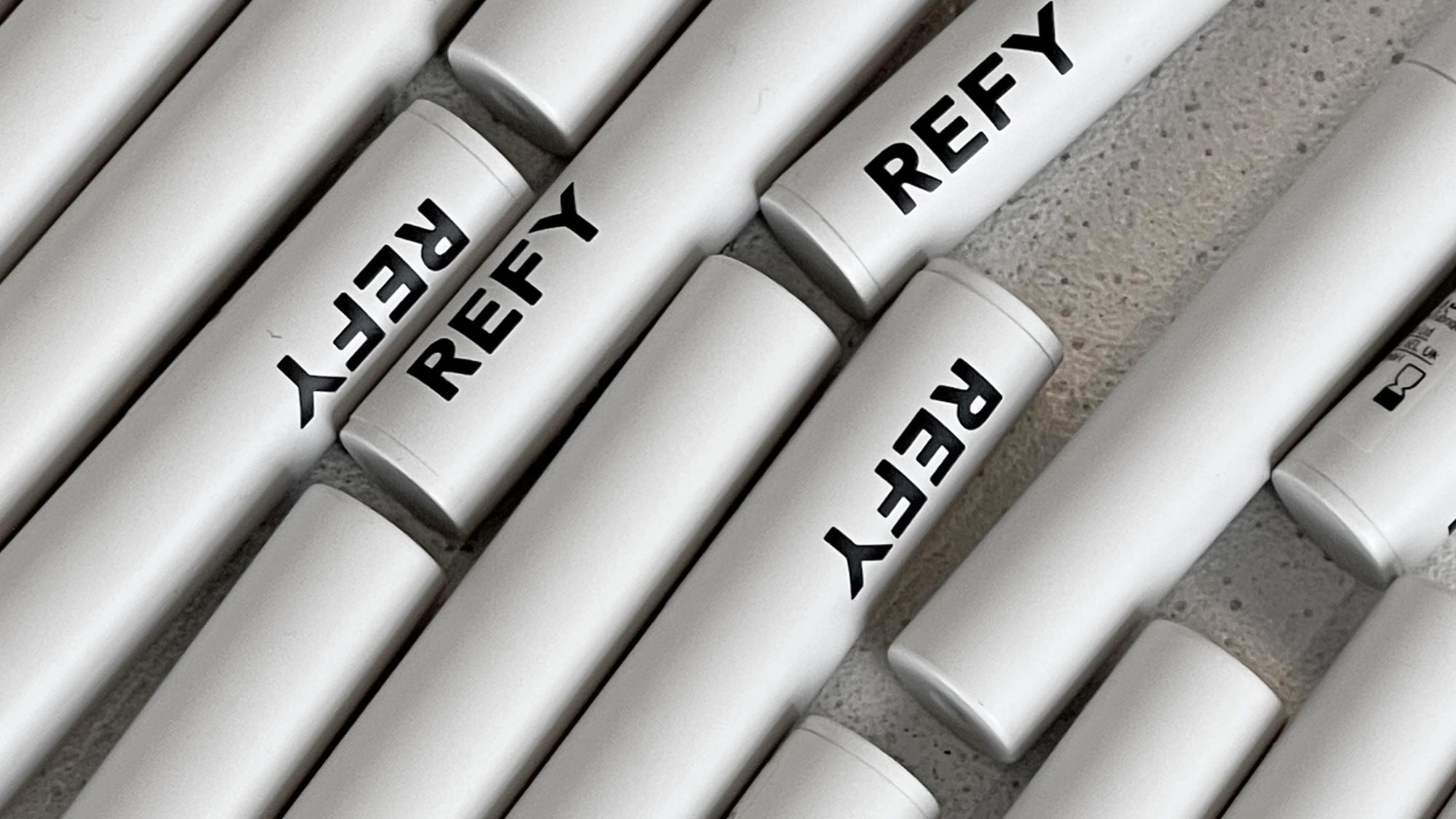 Silver cylindrical tubes with 'REFY' printed on them are arranged diagonally on a textured surface.