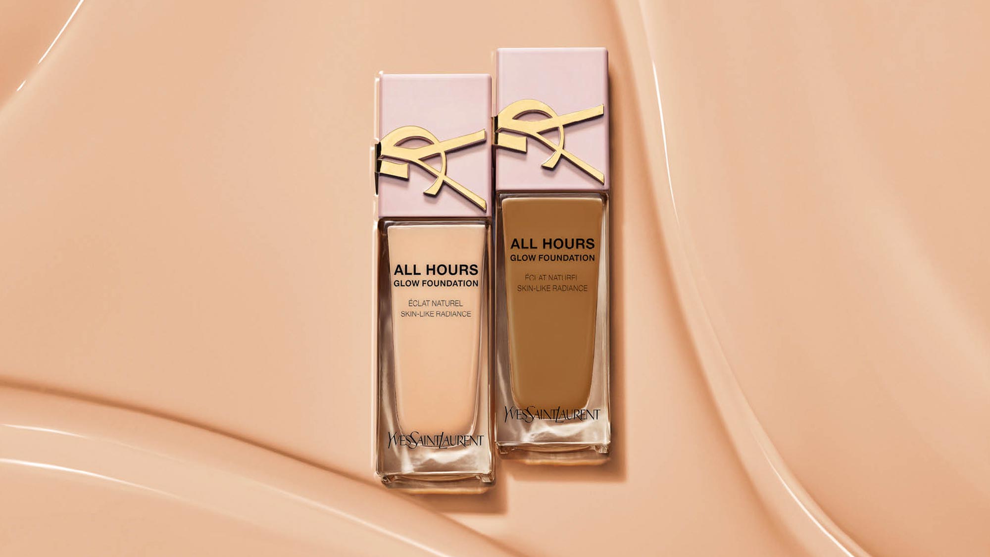 Two bottles of foundation with pink caps and a gold logo on a smooth, beige background.