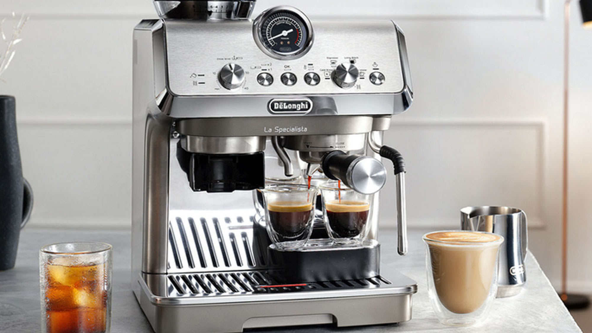 A stainless steel espresso machine with two espresso shots brewing, placed on a kitchen counter with coffee cups nearby.