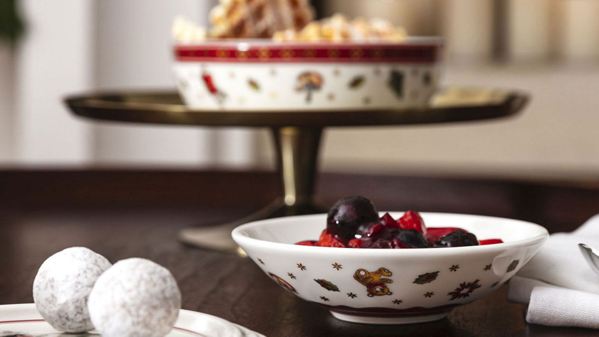 Festive bowls with cookies and fruits, surrounded by lit candles, create a cozy, holiday atmosphere.