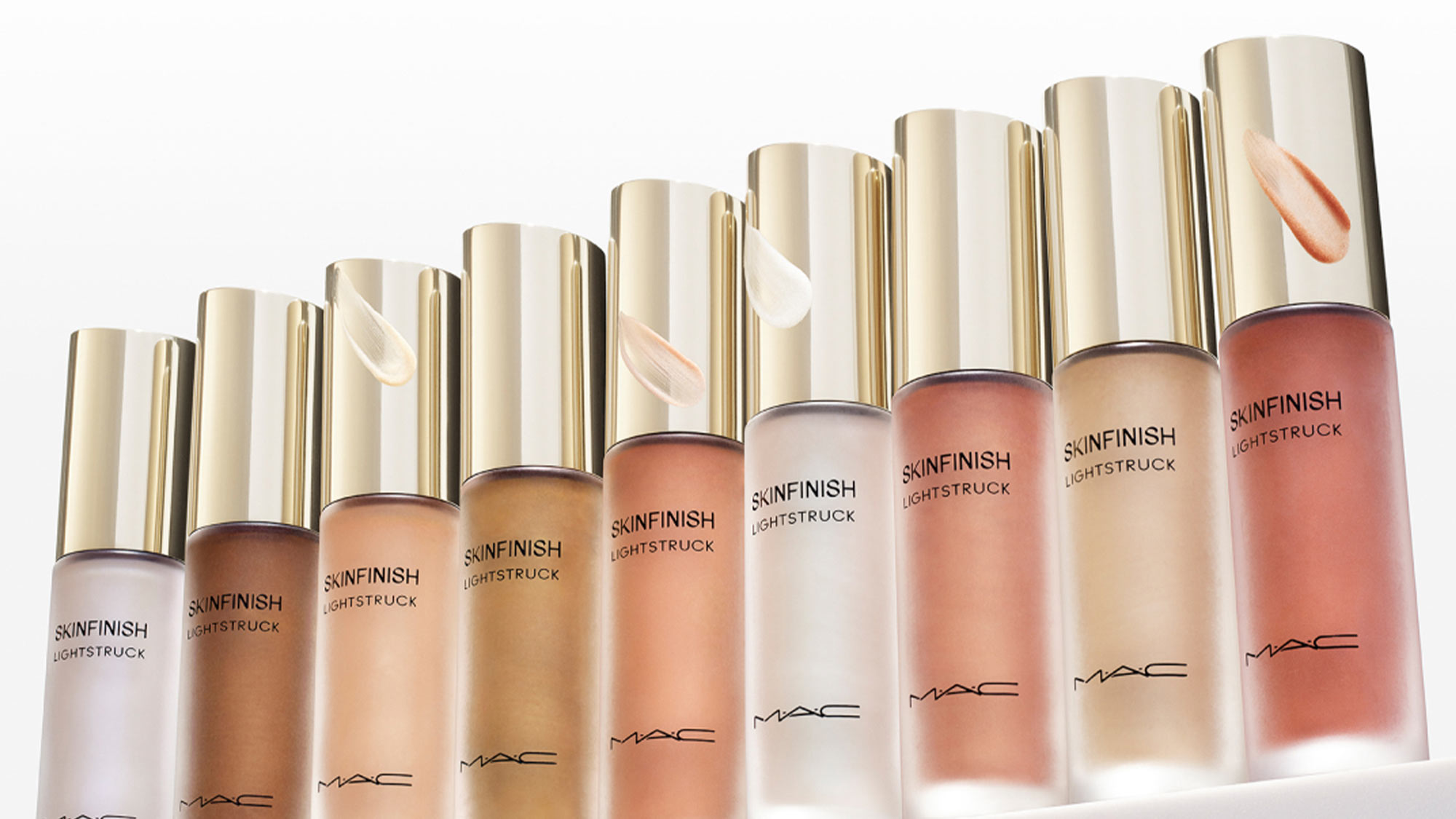 A row of makeup bottles with gold caps, labeled 'SUNFINISH LUSTRE STRUCK,' featuring various shades of liquid on a white background.