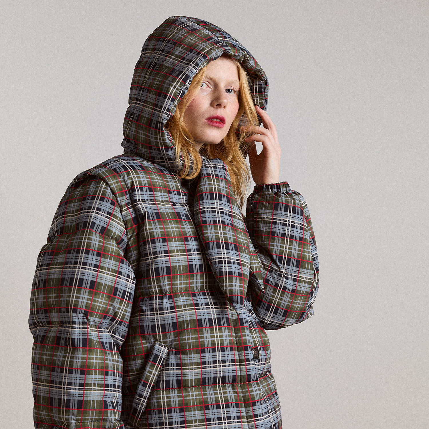 Person wearing a plaid puffer jacket and hood, with a thoughtful expression.
