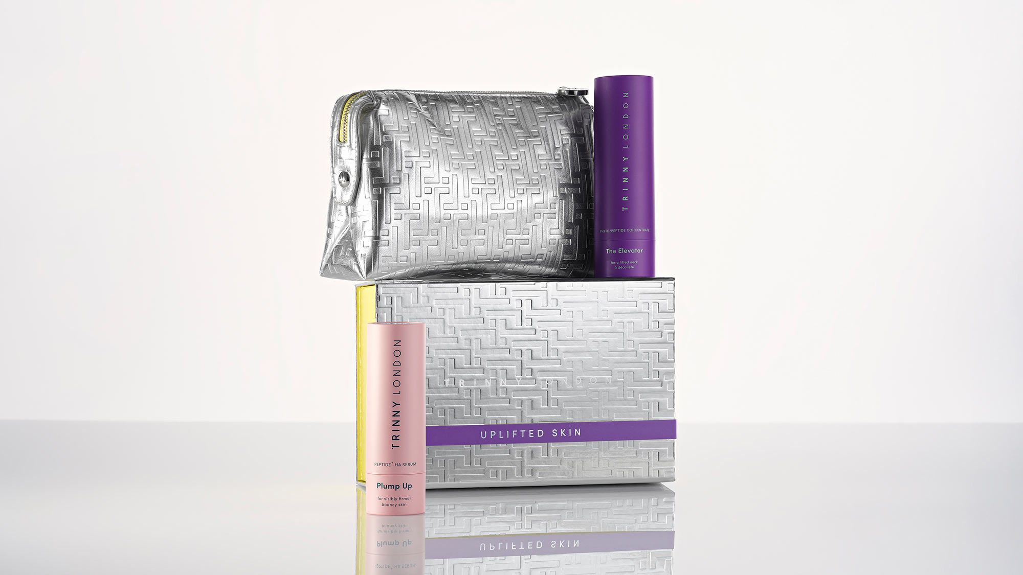 Skincare products with a metallic silver pouch and two cylindrical containers on a reflective surface.