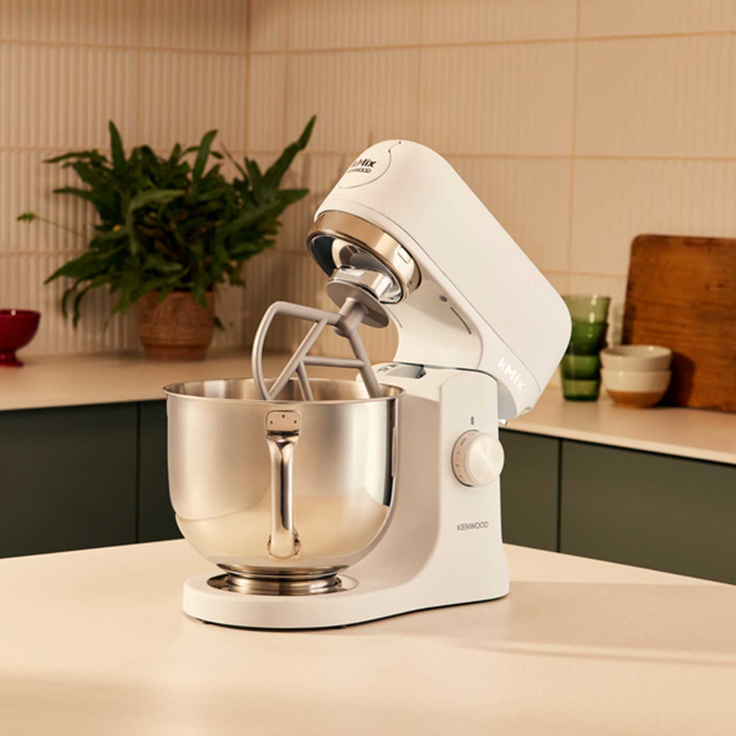 A kitchen with a white stand mixer on the countertop, surrounded by utensils, plants, and kitchenware.
