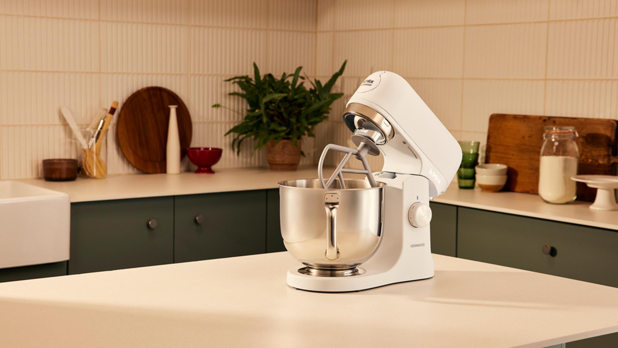 A kitchen with a white stand mixer on the countertop, surrounded by utensils, plants, and kitchenware.