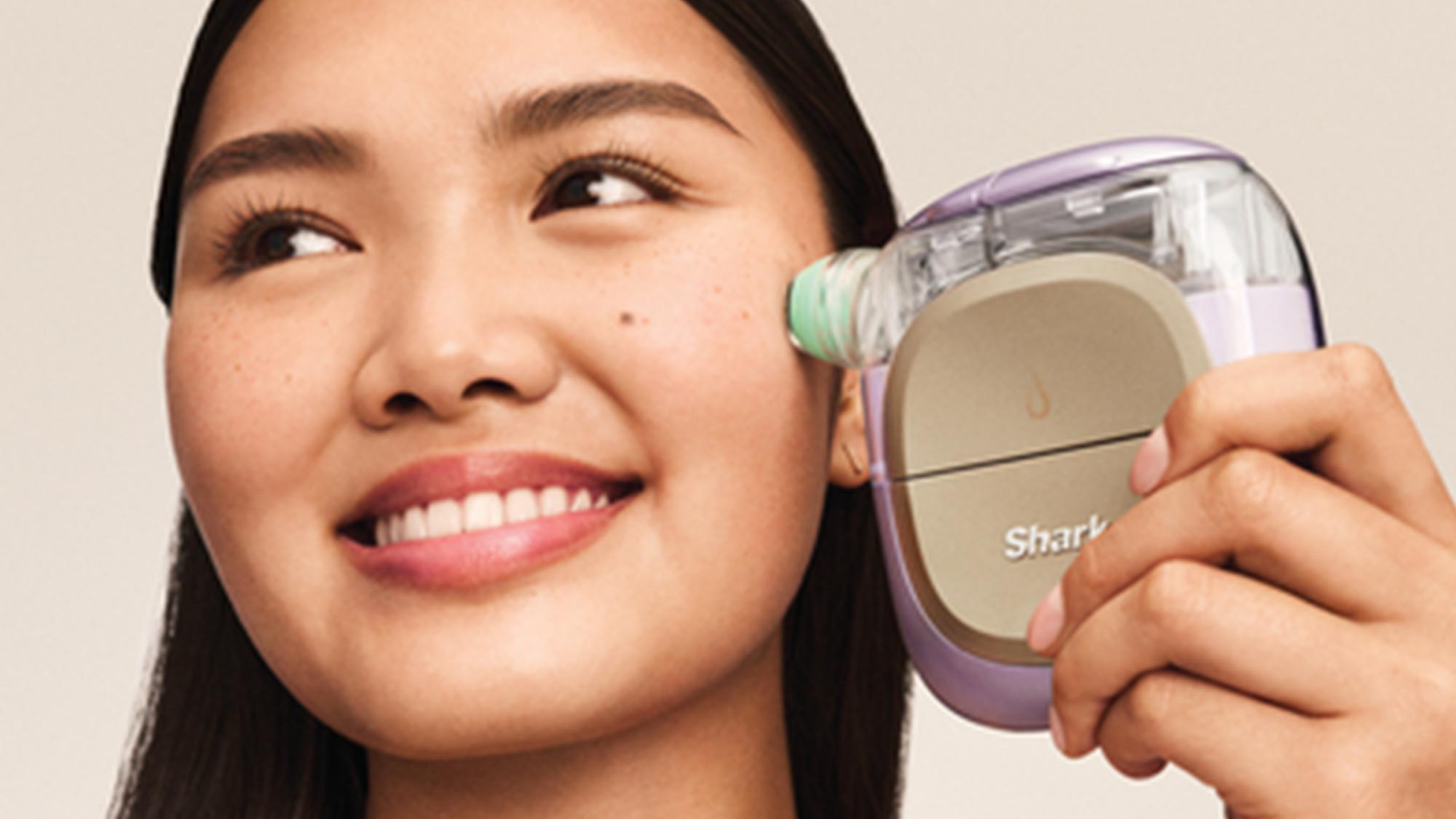 A woman uses a small facial skincare device on her cheek, smiling slightly.
