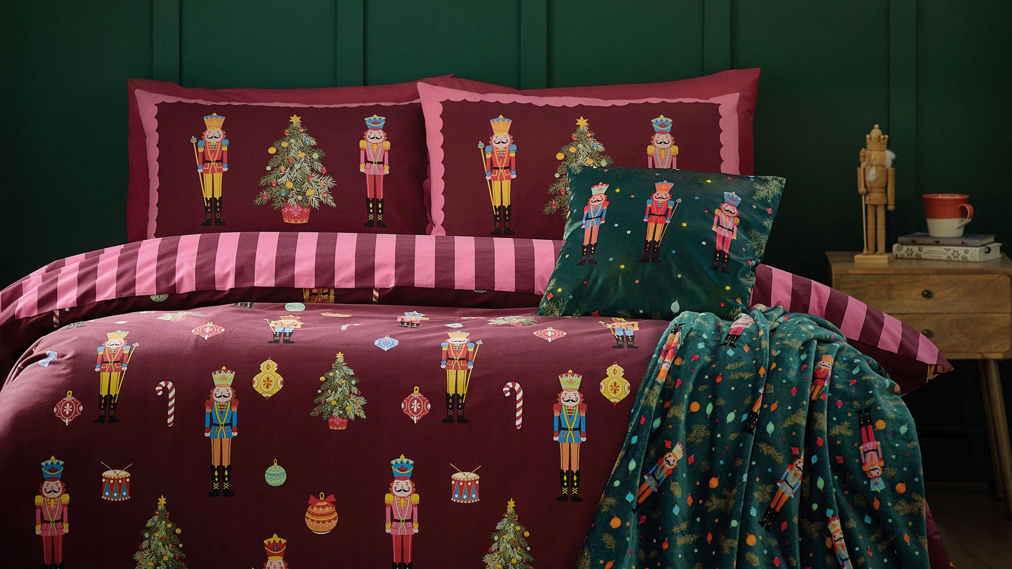 Festive bedroom with nutcracker-themed bedding, dark green walls, string lights, and a cozy blanket draped on the bed.