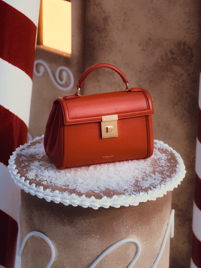 A red handbag with a gold clasp is placed on a snowy, decorative stand resembling a cake, surrounded by candy cane patterns.
