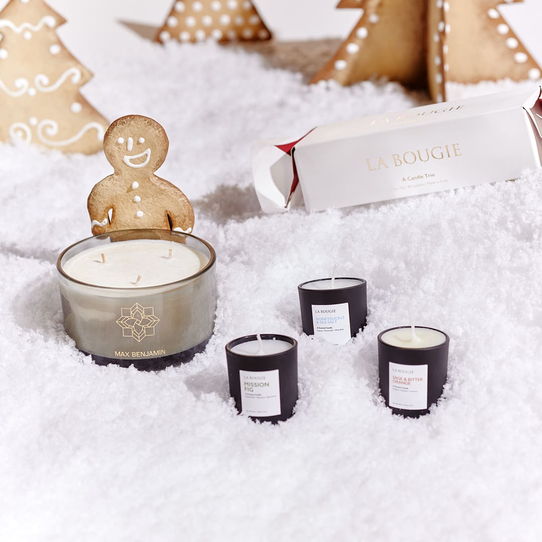 Candles and a gingerbread man on snow-like surface, surrounded by gingerbread trees and a La Bougie package.