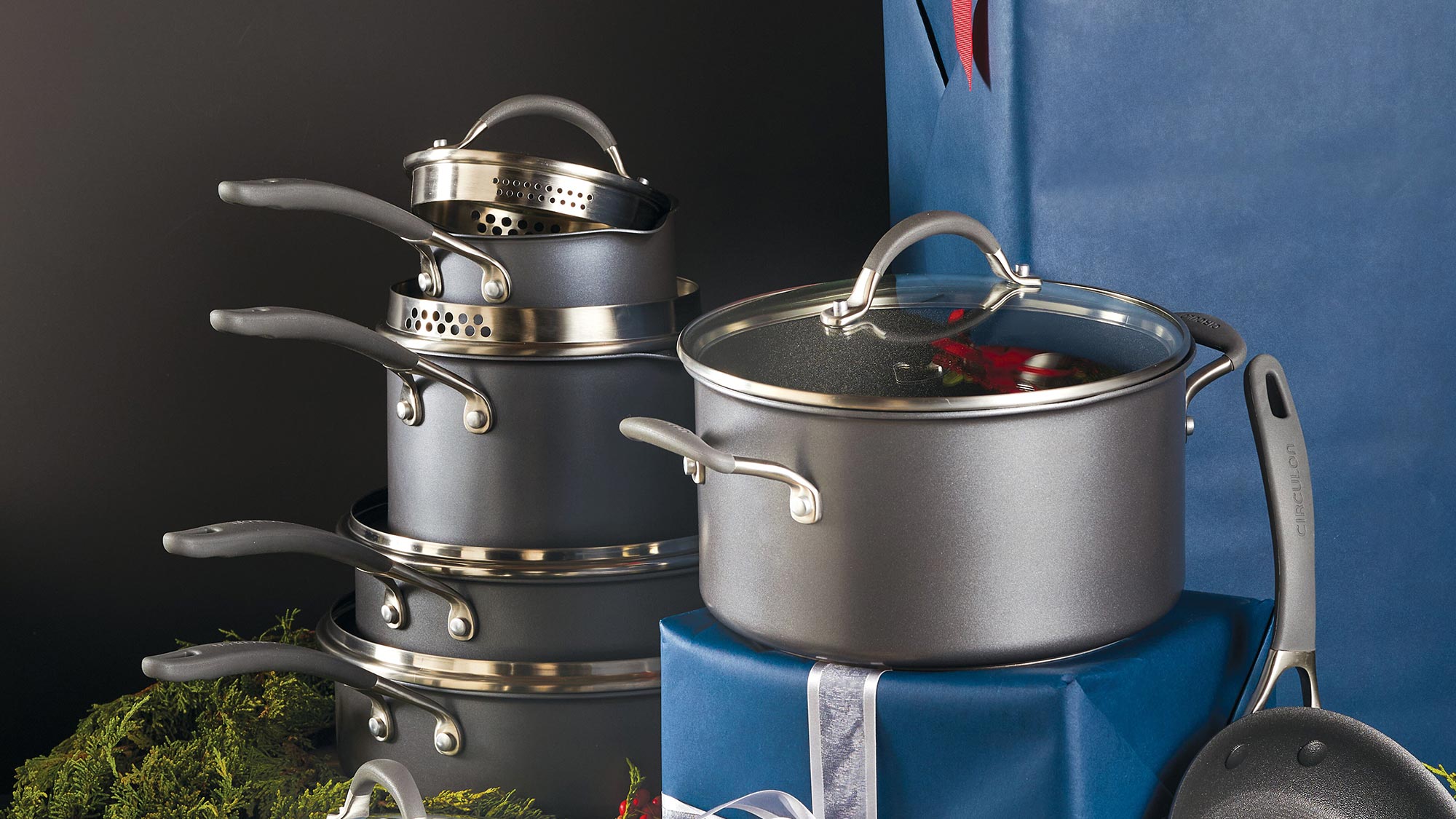 Cookware set with utensils, wrapped blue gifts, and holiday decorations on a dark background.