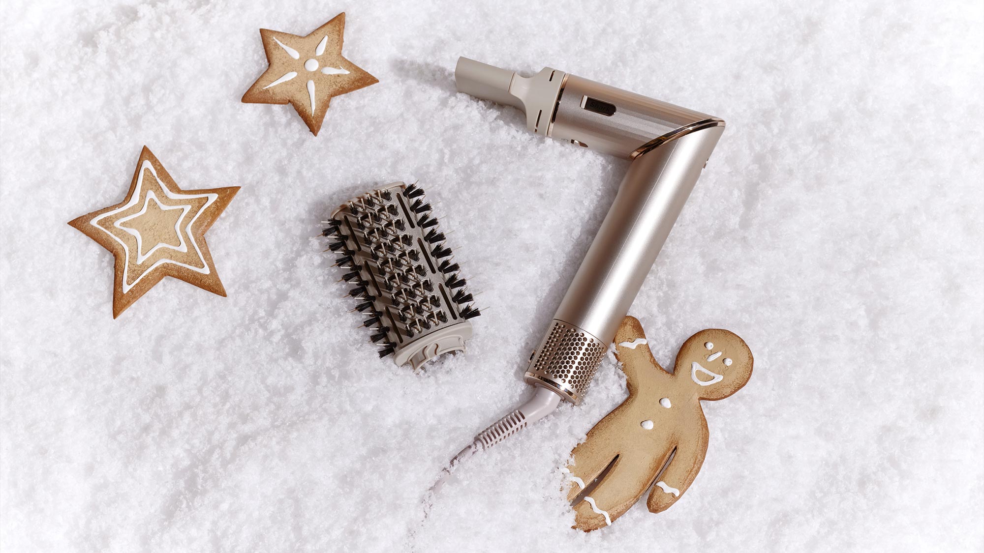 A hairdryer and a brush are placed on faux snow with star-shaped cookies and a gingerbread man.