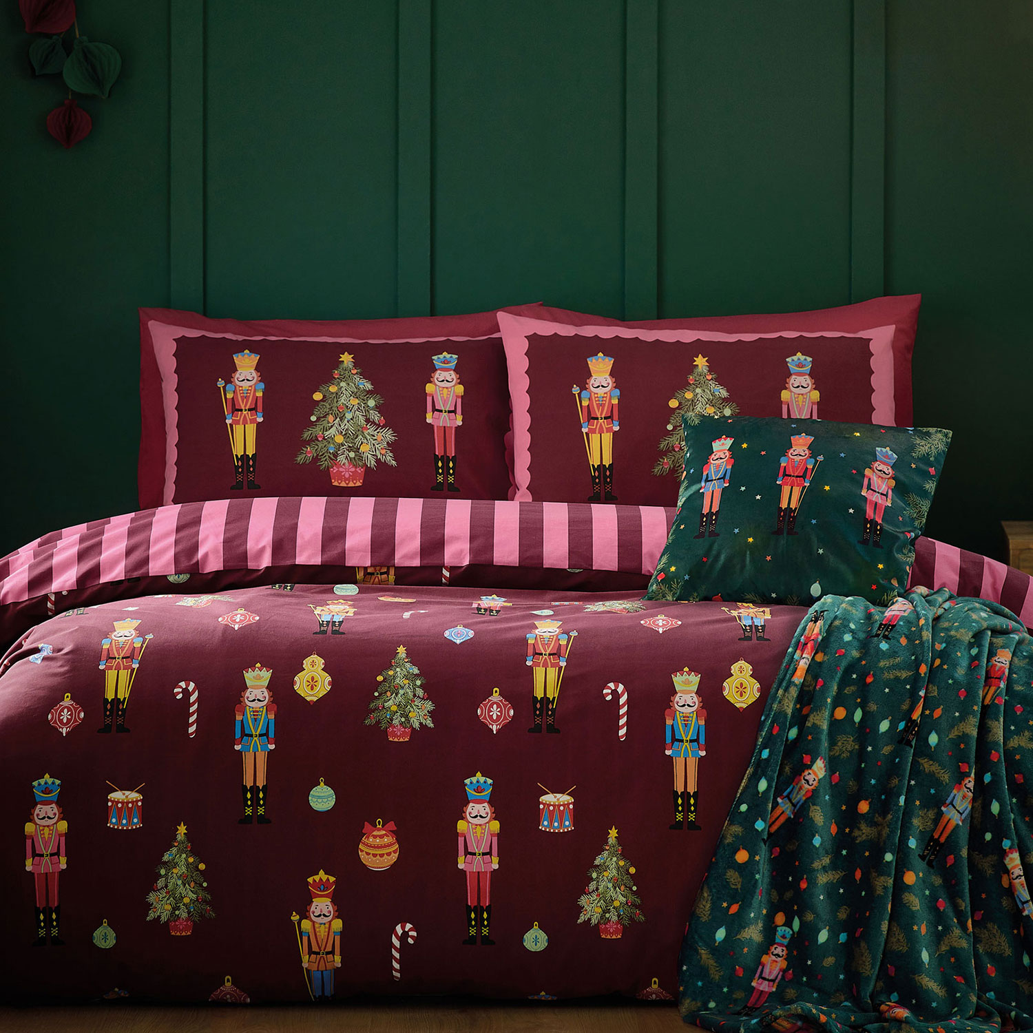 Festive bedroom with nutcracker-themed bedding, dark green walls, string lights, and a cozy blanket draped on the bed.