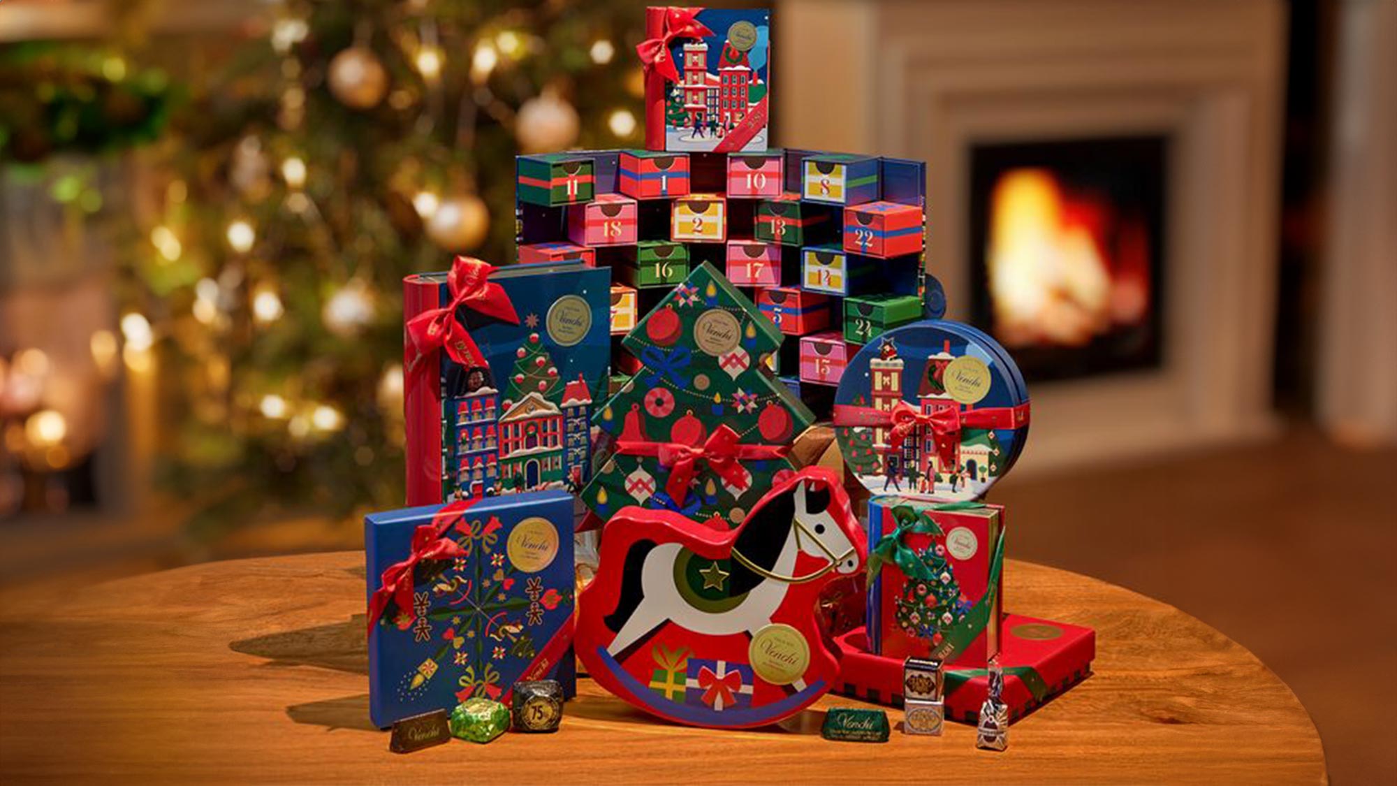 A festive display features colorful gift boxes, a toy horse, and a hand placing a star. A Christmas tree and fireplace are in the background.