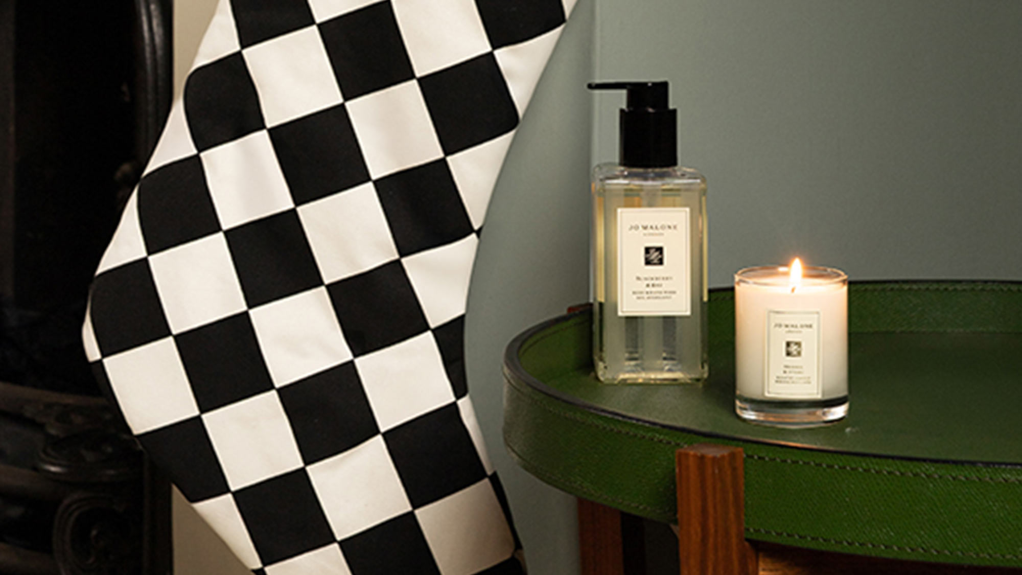 A black-and-white checkered cloth, a candle, and a soap dispenser are placed on a green table.