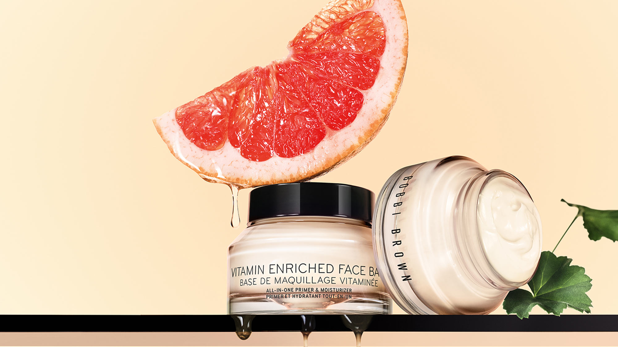 Two face cream jars, one open, with a grapefruit slice and green leaves on a light background.