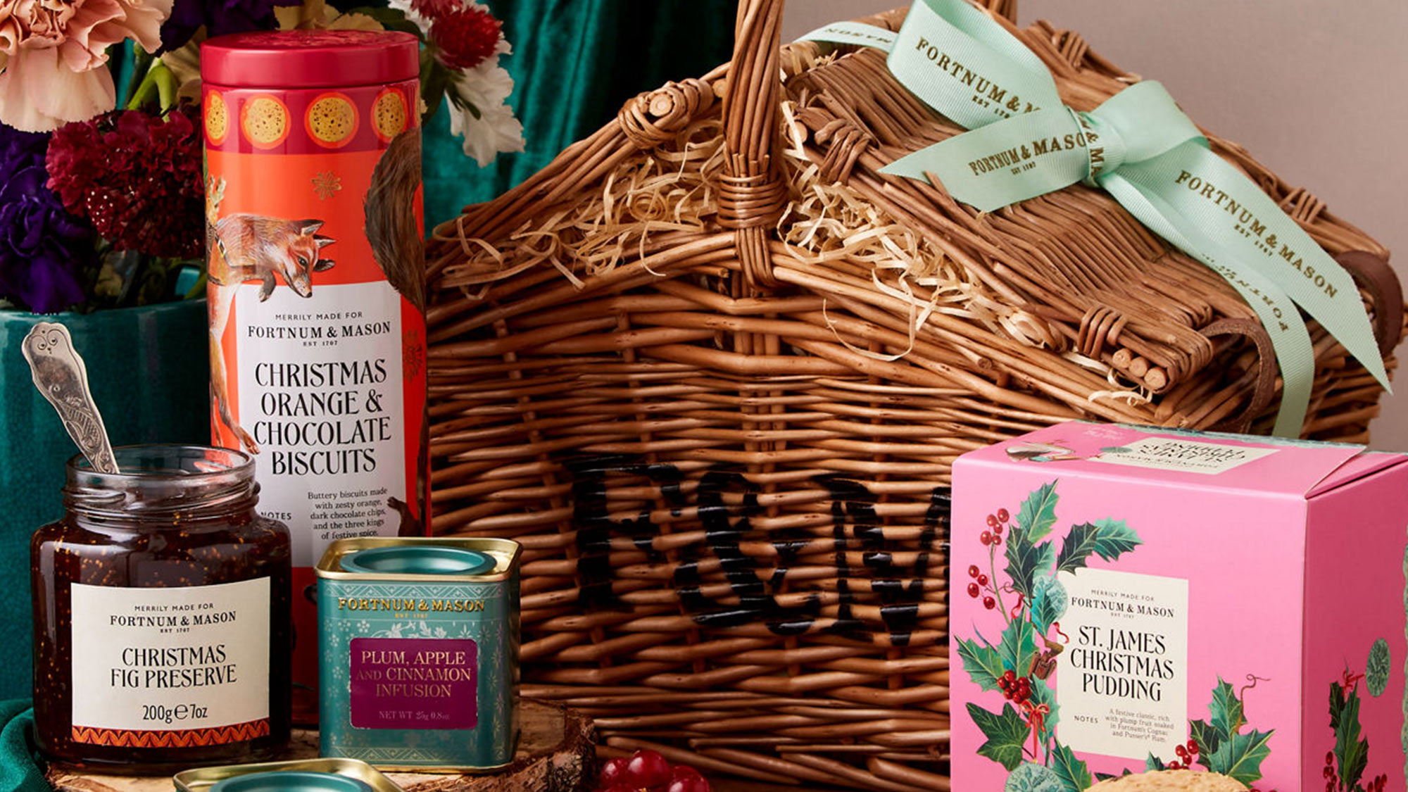 Festive hamper with a basket, floral arrangement, Christmas-themed foods, and decorative products on display.