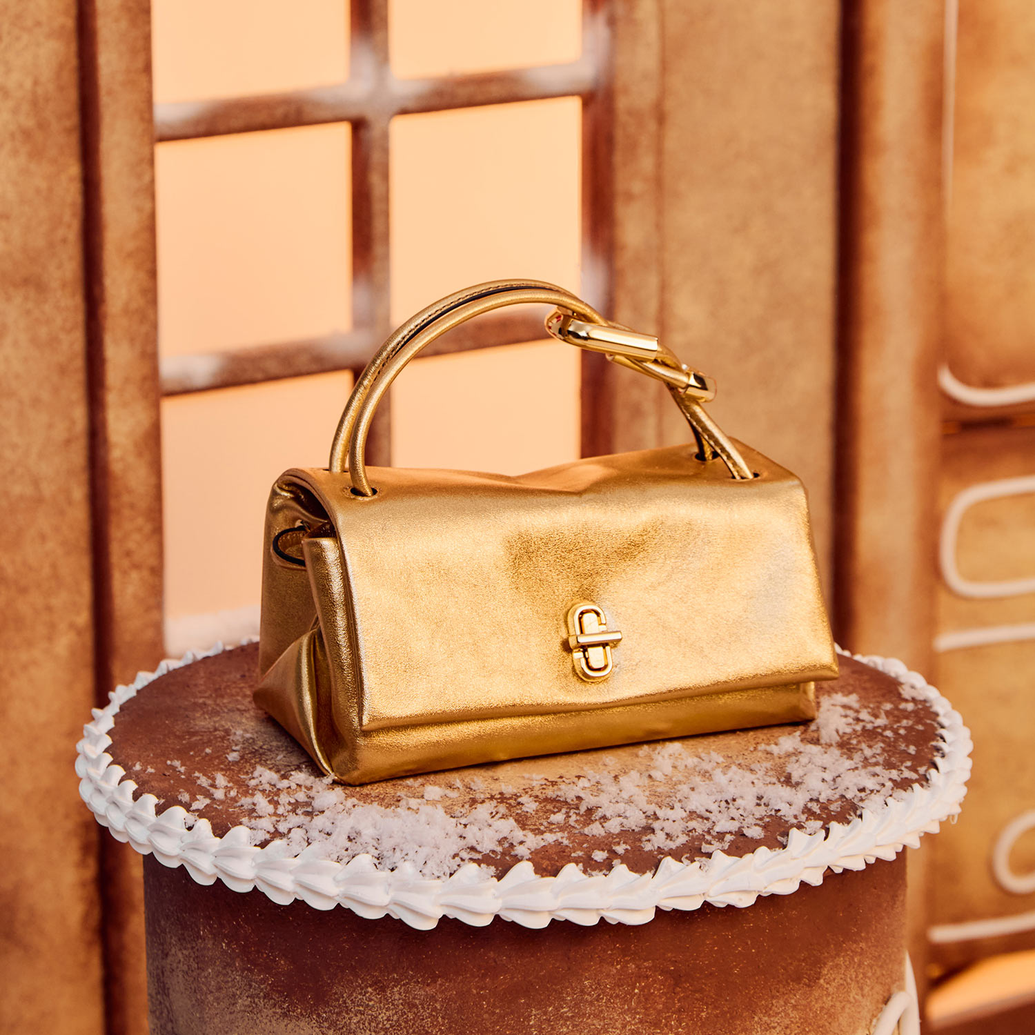 A gold handbag sits on a cake-like stand in a warm, decorated setting with faux window and icing details.