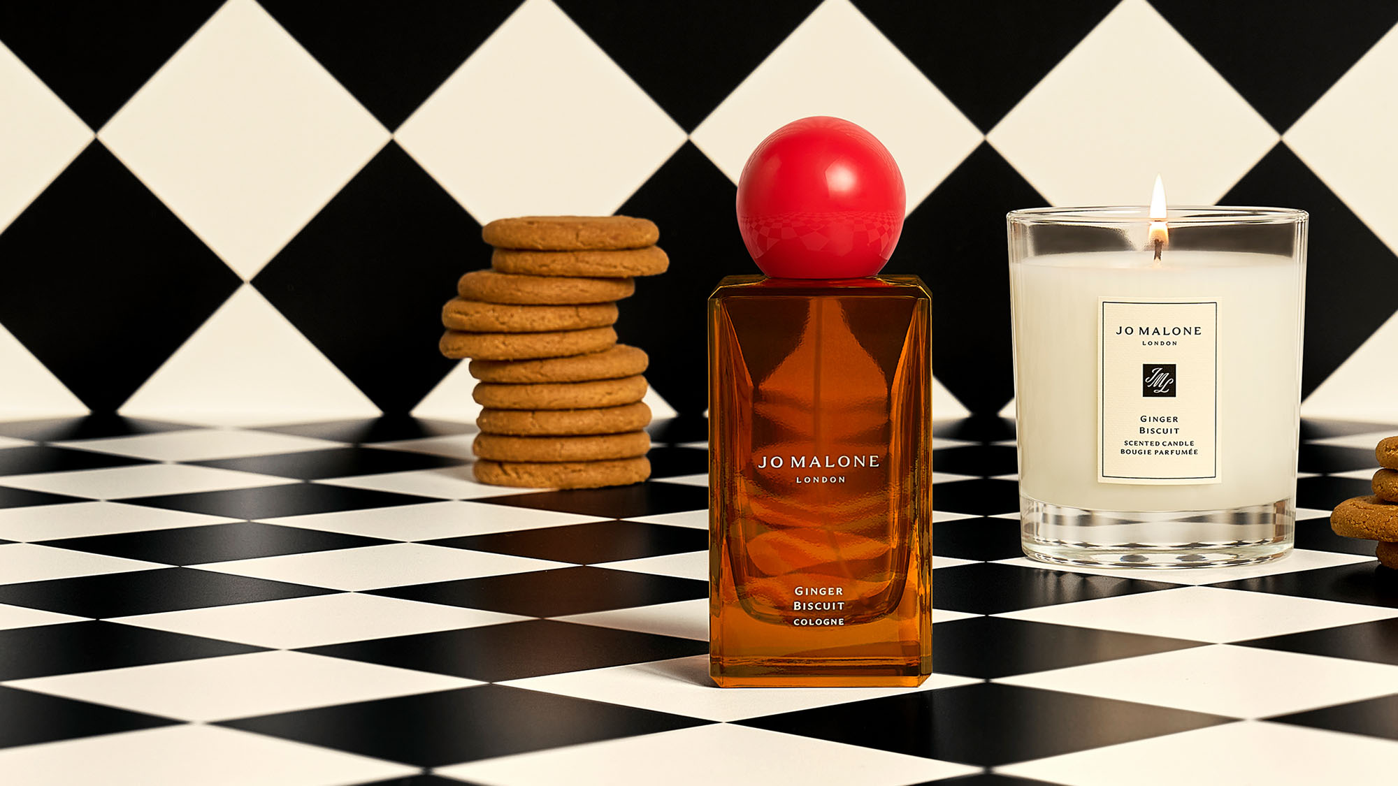 Perfume and candle on a black-and-white checkered surface, surrounded by cookie stacks.