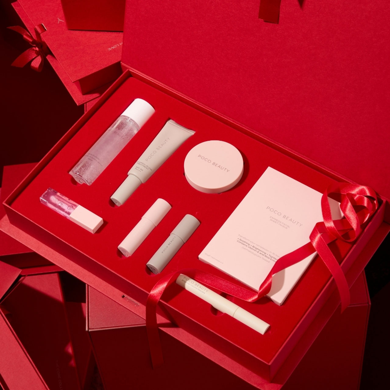 A red gift box containing various beauty products, including bottles, tubes, and a compact, with a red ribbon accent.