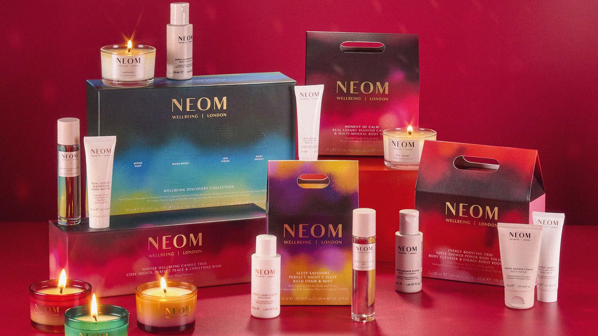 Neom products, including candles and skincare, arranged on a red surface with a mirrored disco ball above.