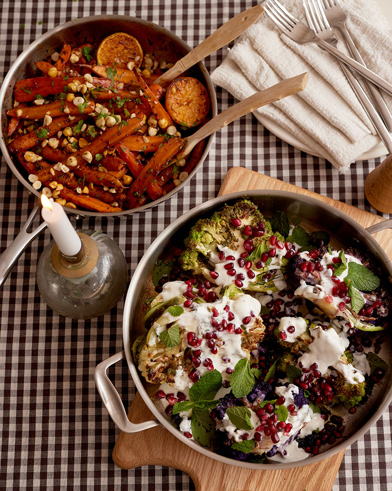 Two dishes on a checkered tablecloth: roasted carrots with corn and herbs, and roasted broccoli with yogurt, pomegranate, and mint.