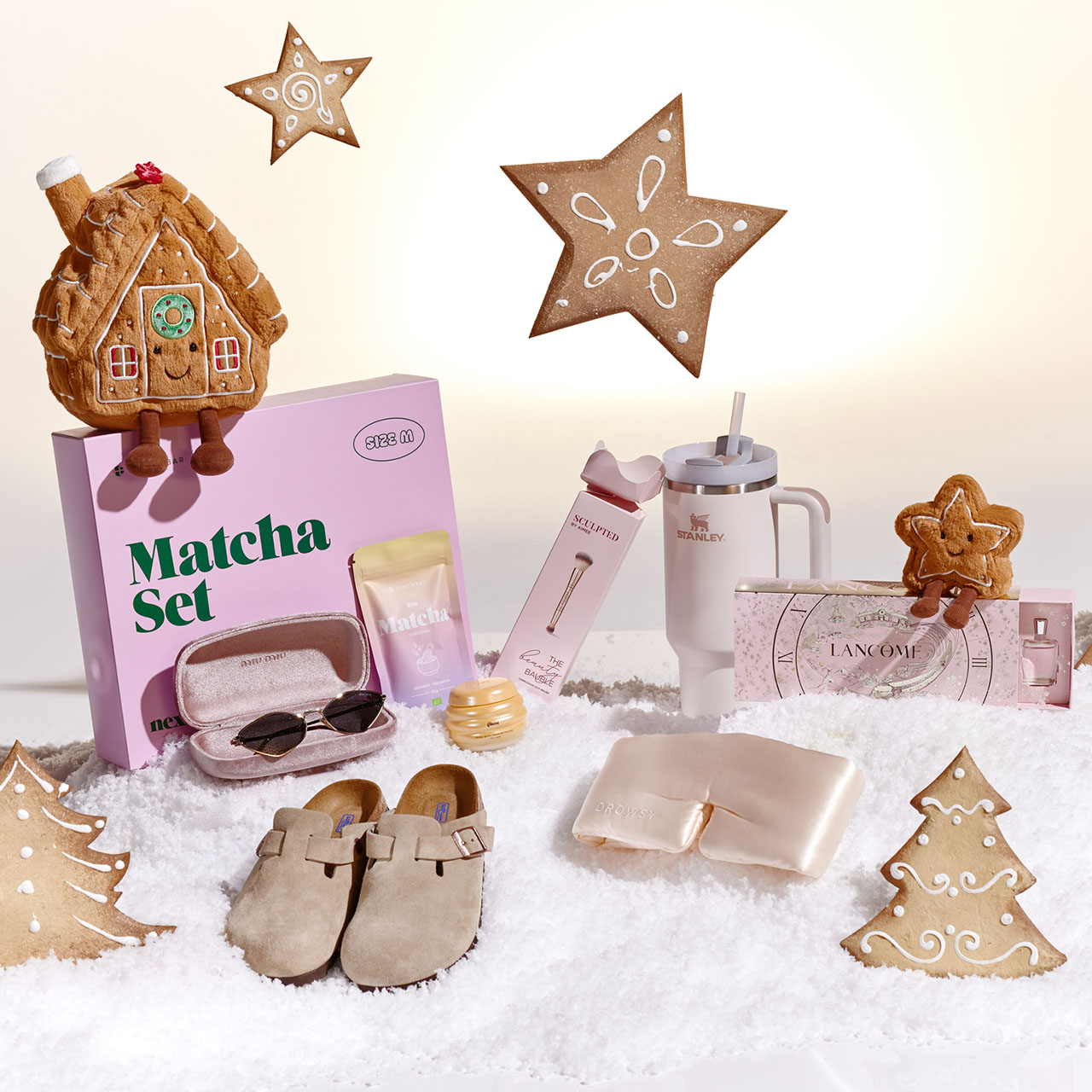 Festive holiday display with gingerbread cookies, matcha set, slippers, and festive decorations on snow.