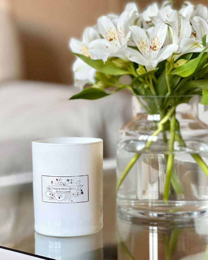 A white candle and a clear vase of white flowers on a glass table.
