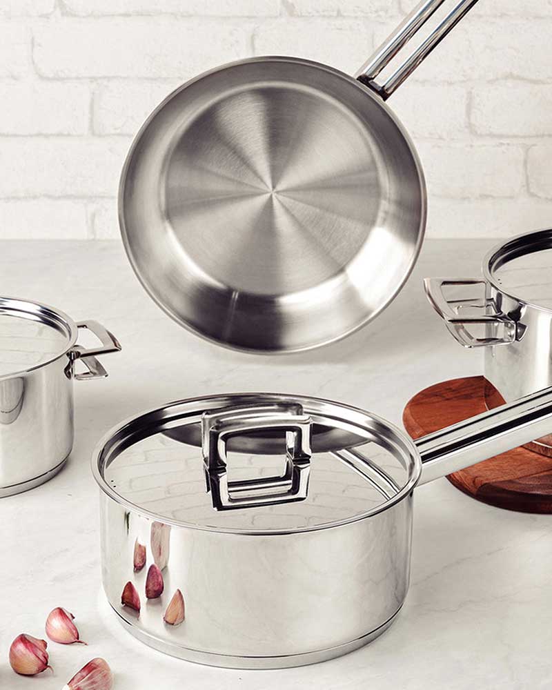 Stainless steel cookware set on a kitchen counter, with garlic cloves nearby.