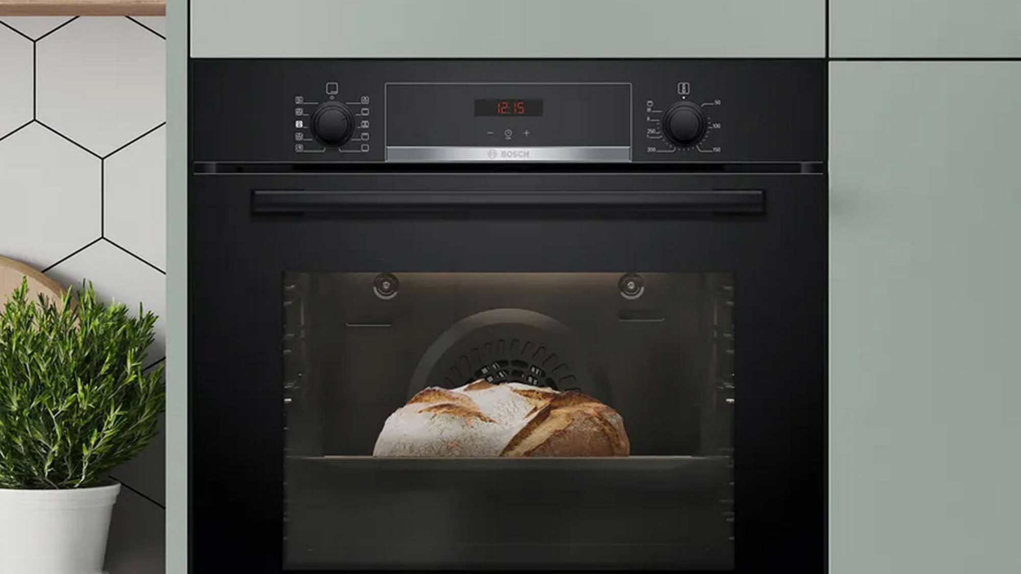 Built-in oven baking bread, next to a geometric-tiled wall and potted plant.