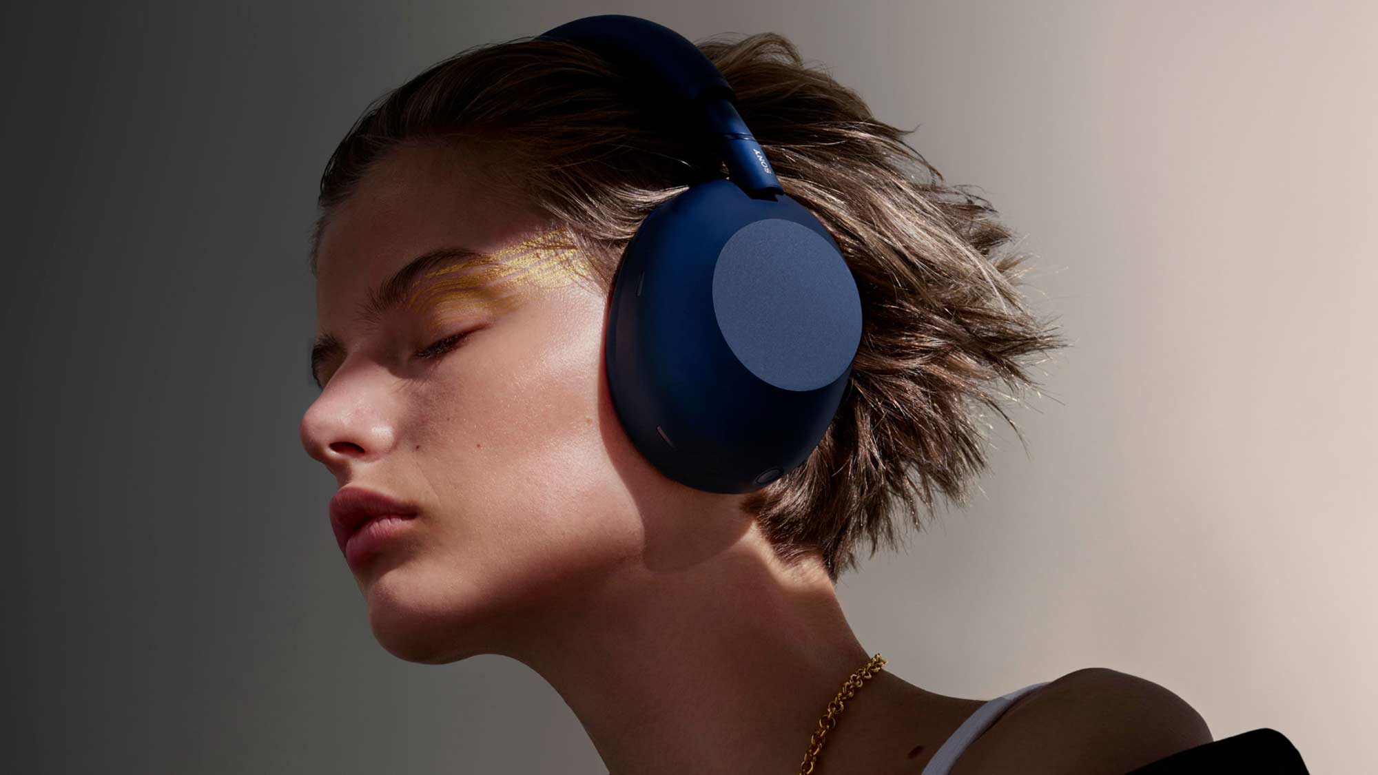 A person with short hair wearing large blue headphones with closed eyes, bathed in soft lighting.
